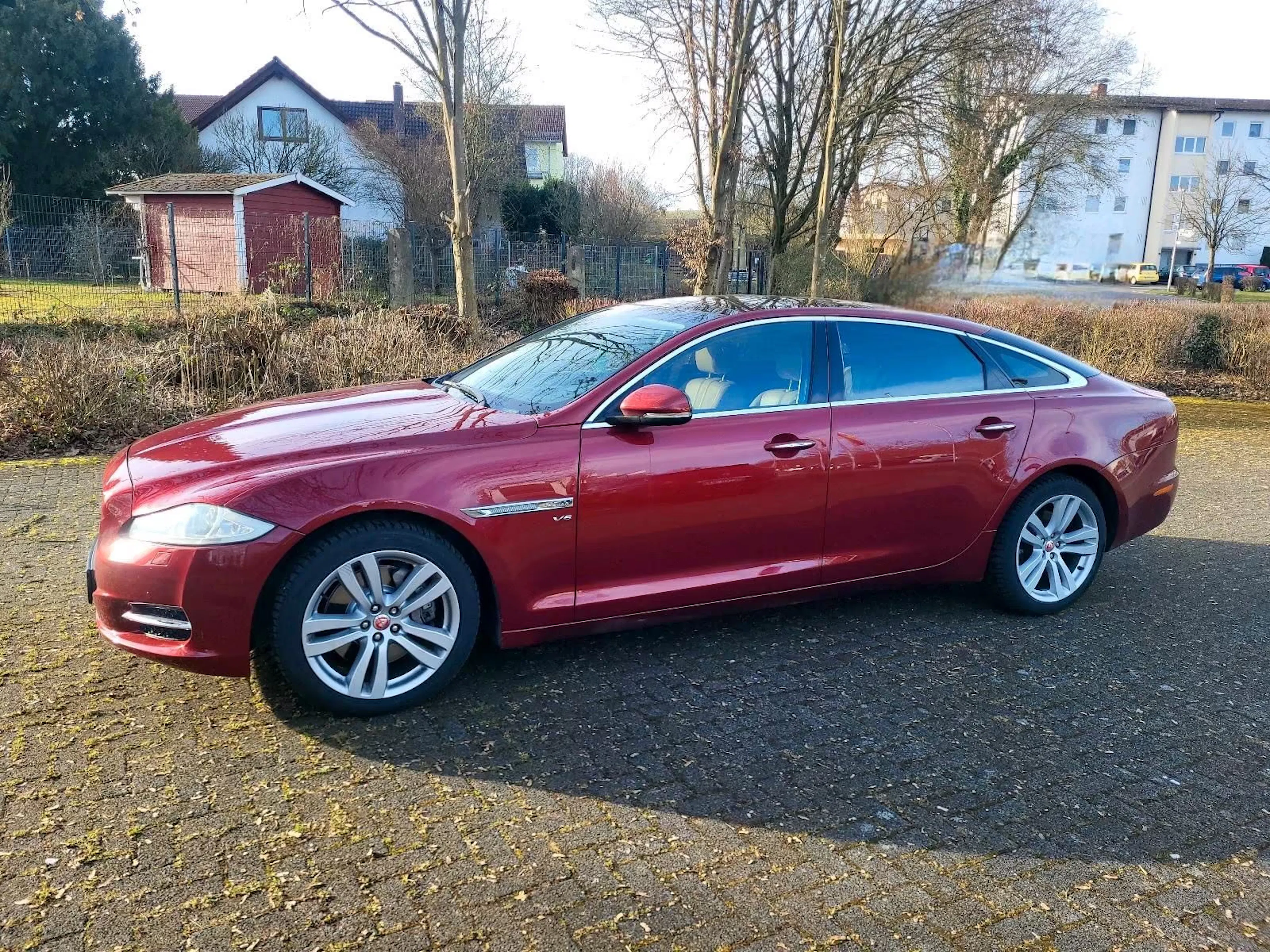 Ein roter Jaguar XJ X351 steht vor einem Familienhaus.