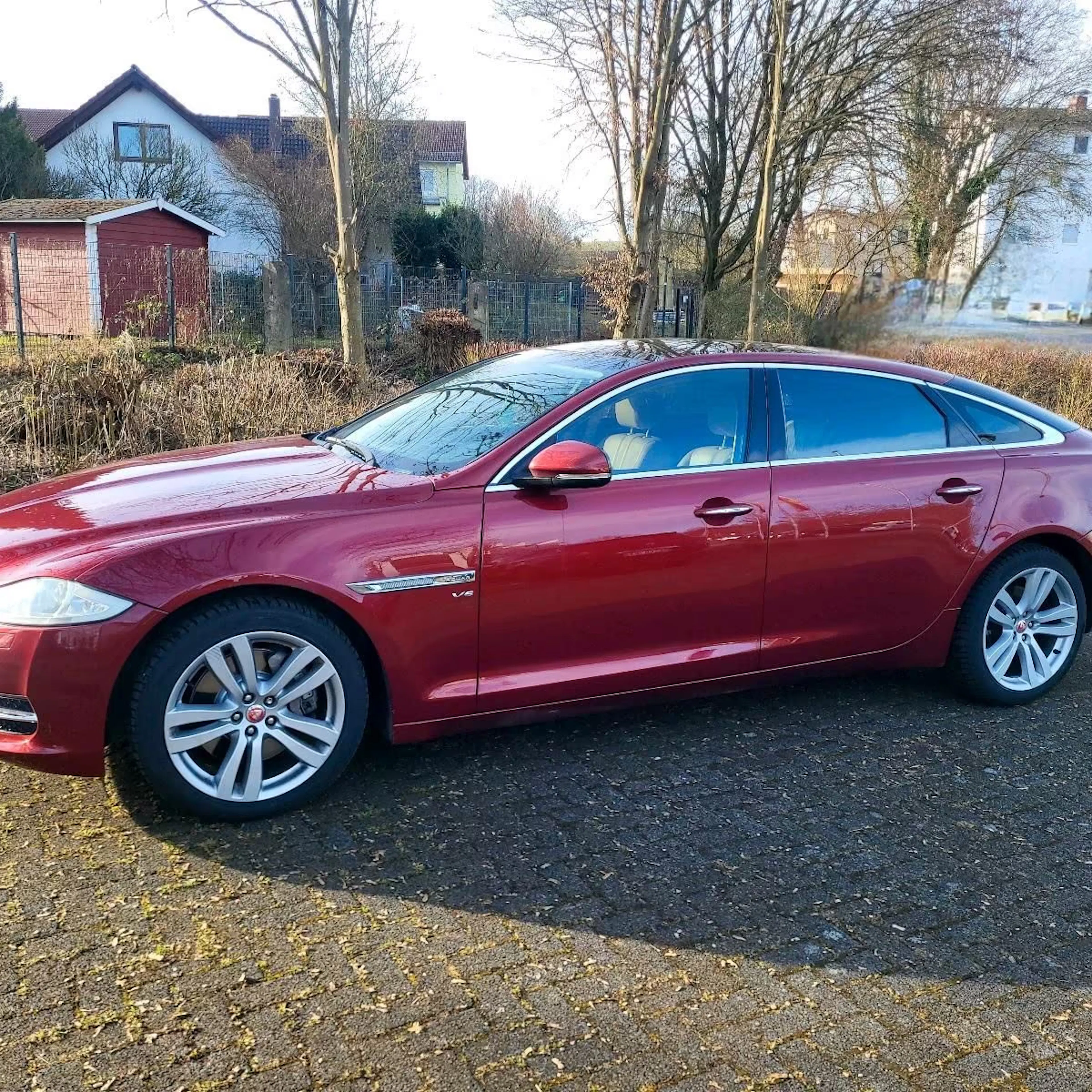 Ein roter Jaguar XJ X351 steht vor einem Familienhaus.