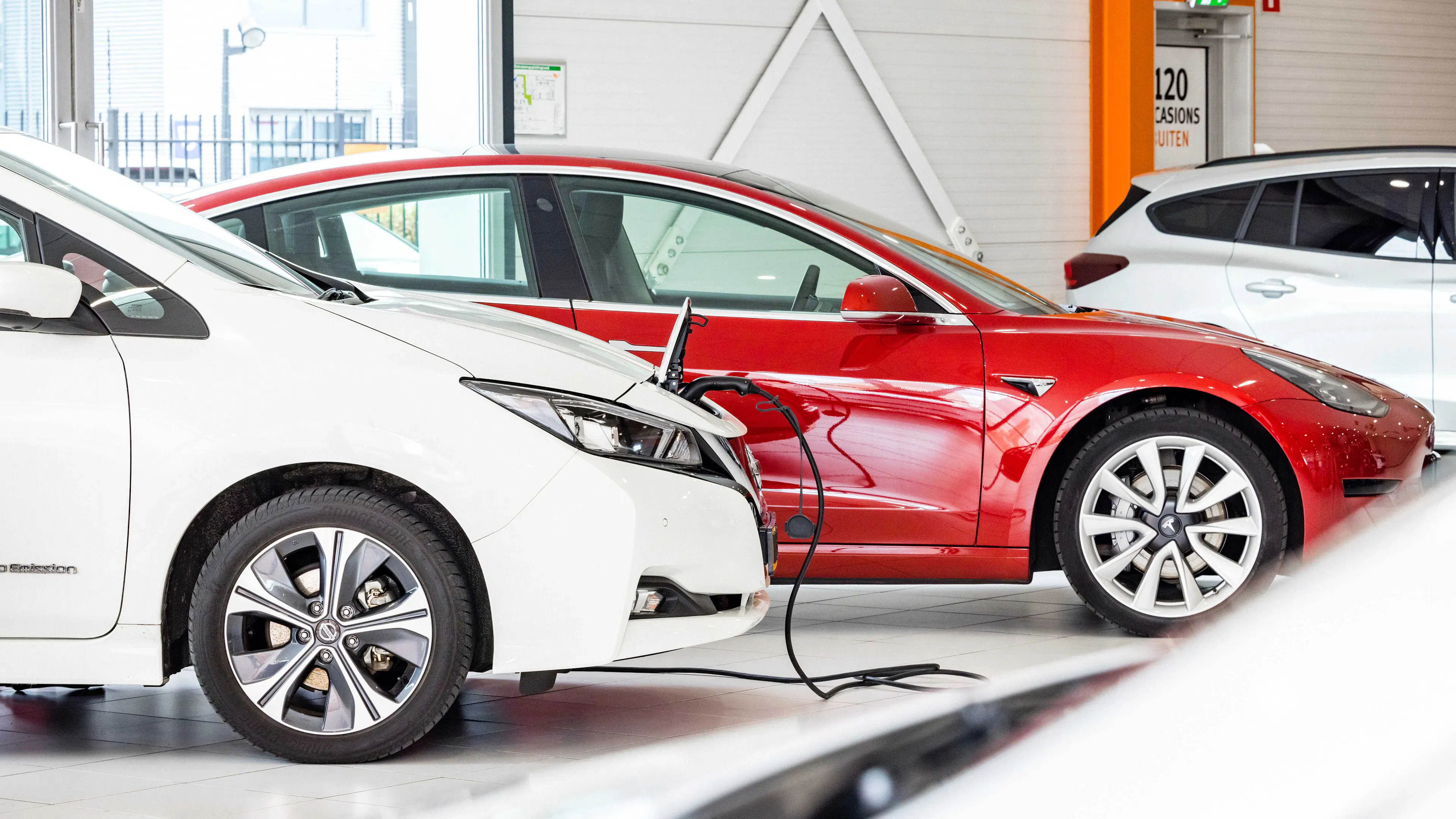 Zwei Elektroautos (eins rot, eins weiß) stehen auf einer Verkaufsfläche.