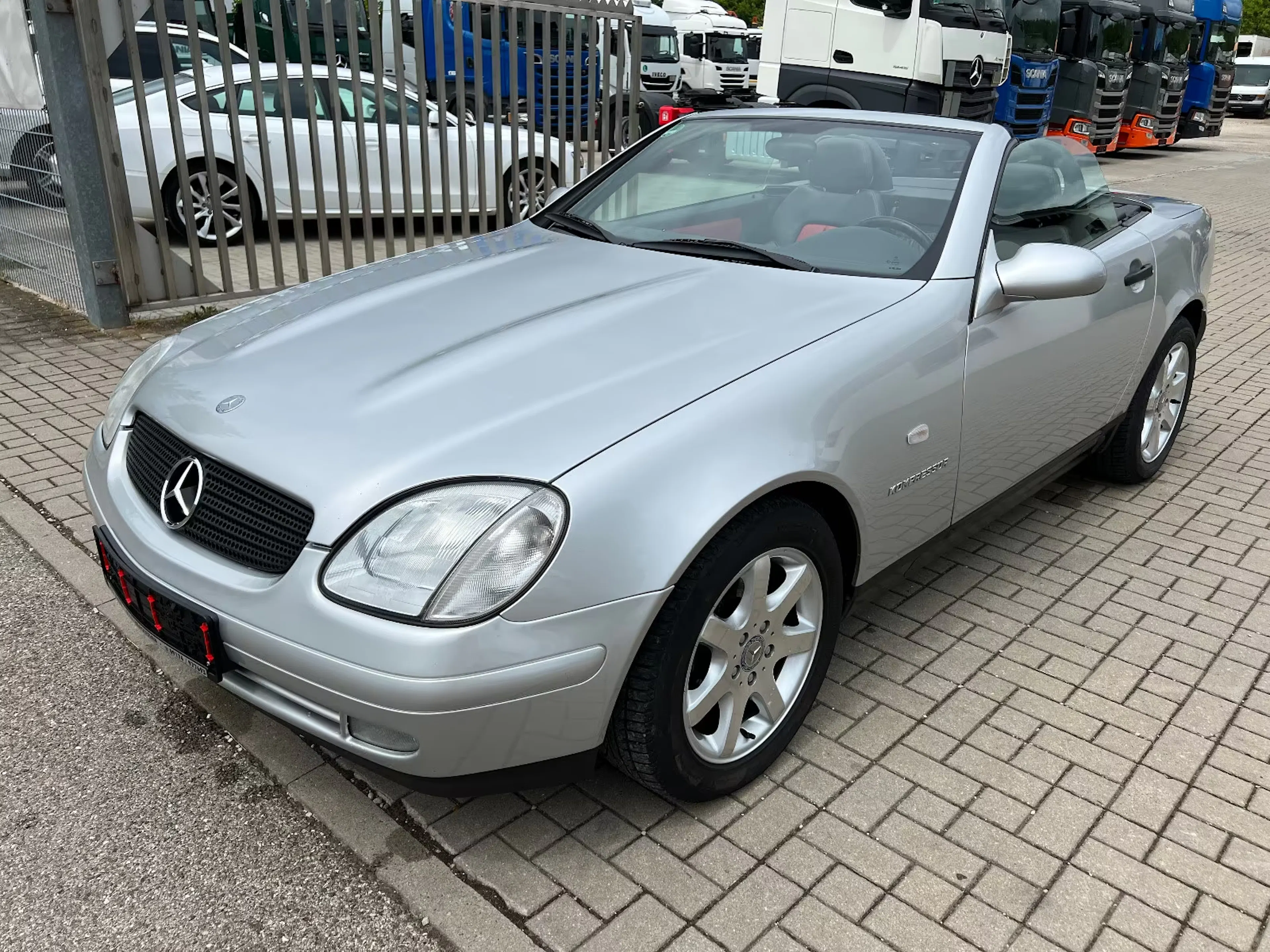 Ein silberner Mercedes-Benz SLK steht auf einem gepflasterten Weg.