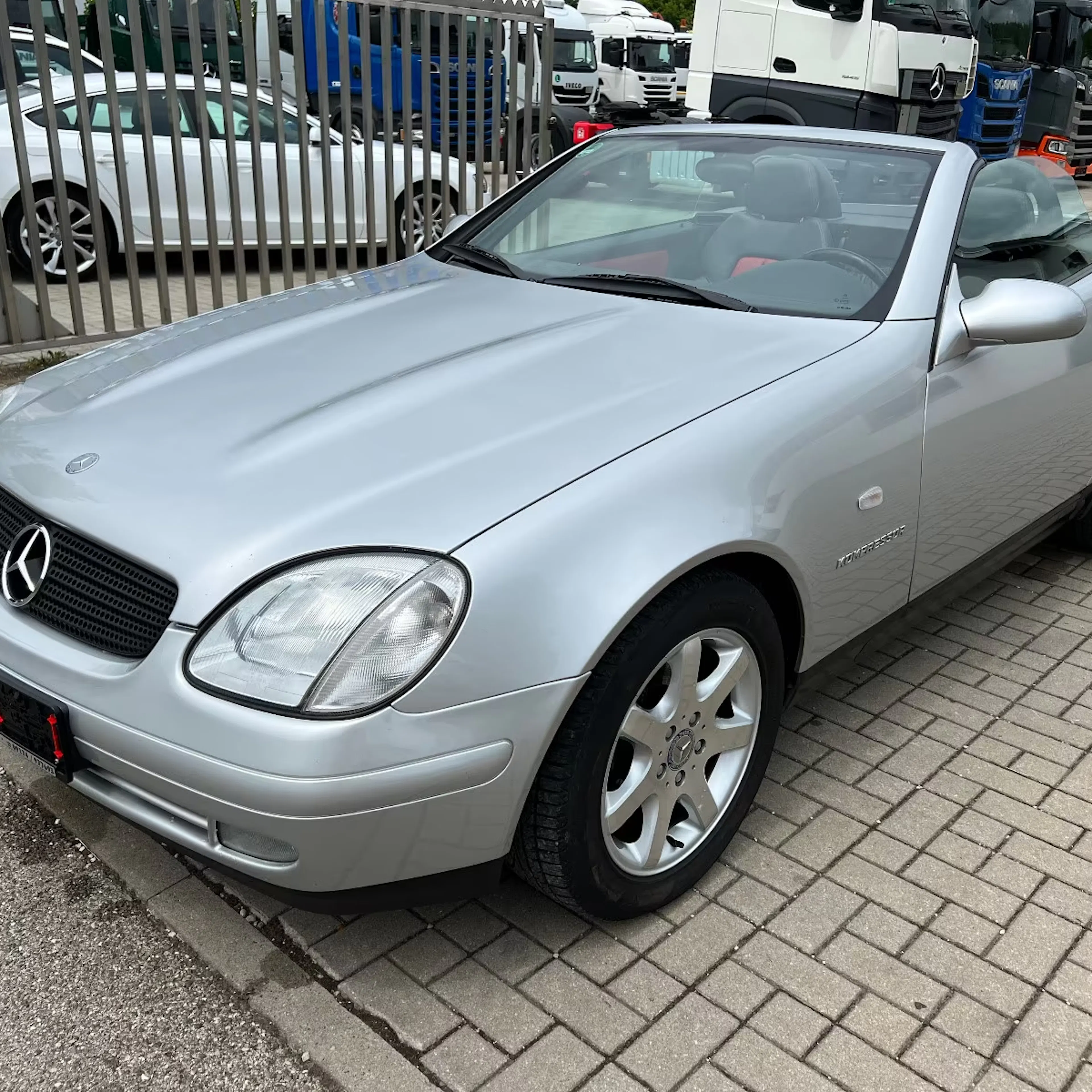 Ein silberner Mercedes-Benz SLK steht auf einem gepflasterten Weg.