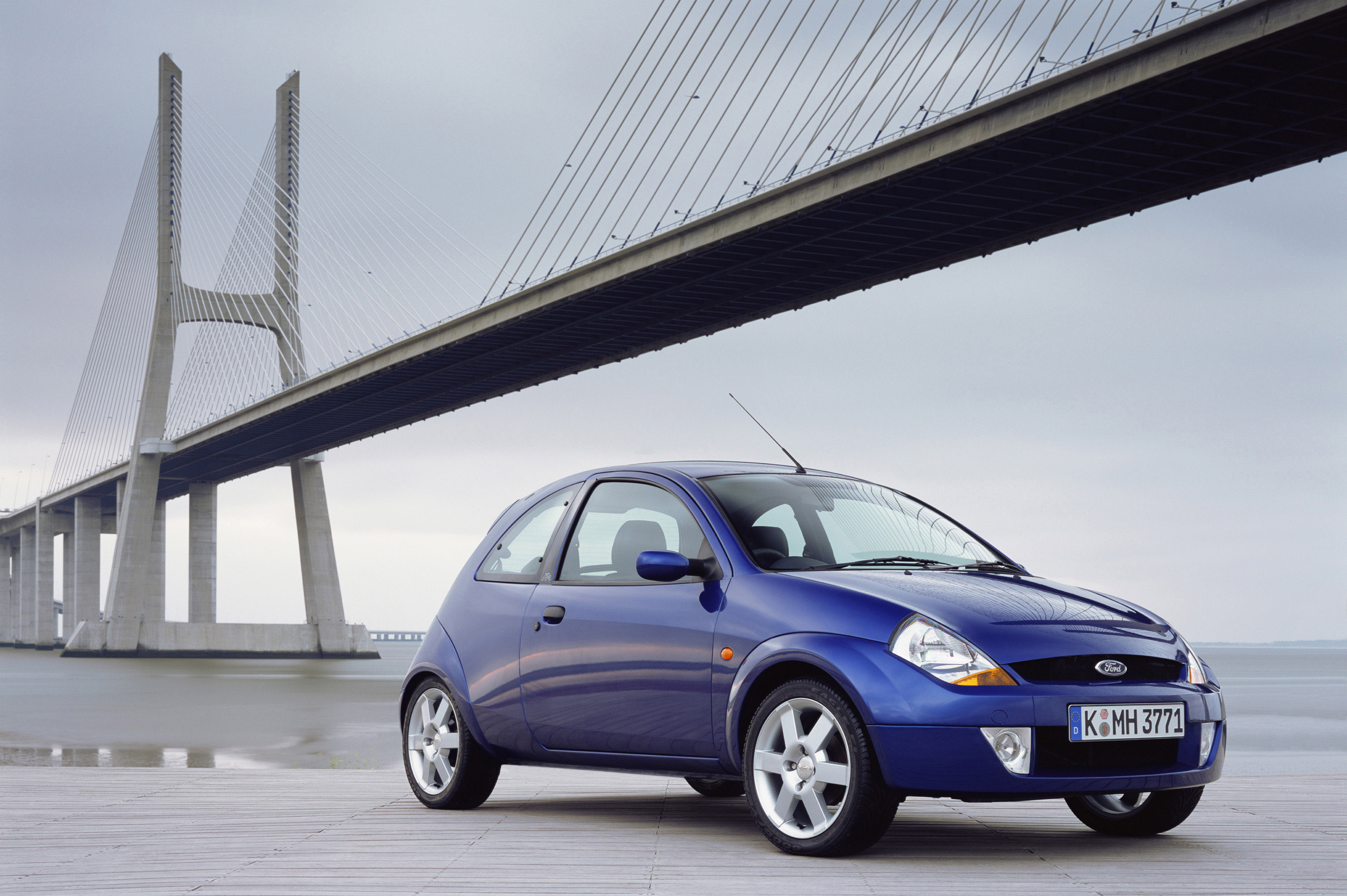 Ein blauer Ford Ka steht vor einer modernen Brücke.