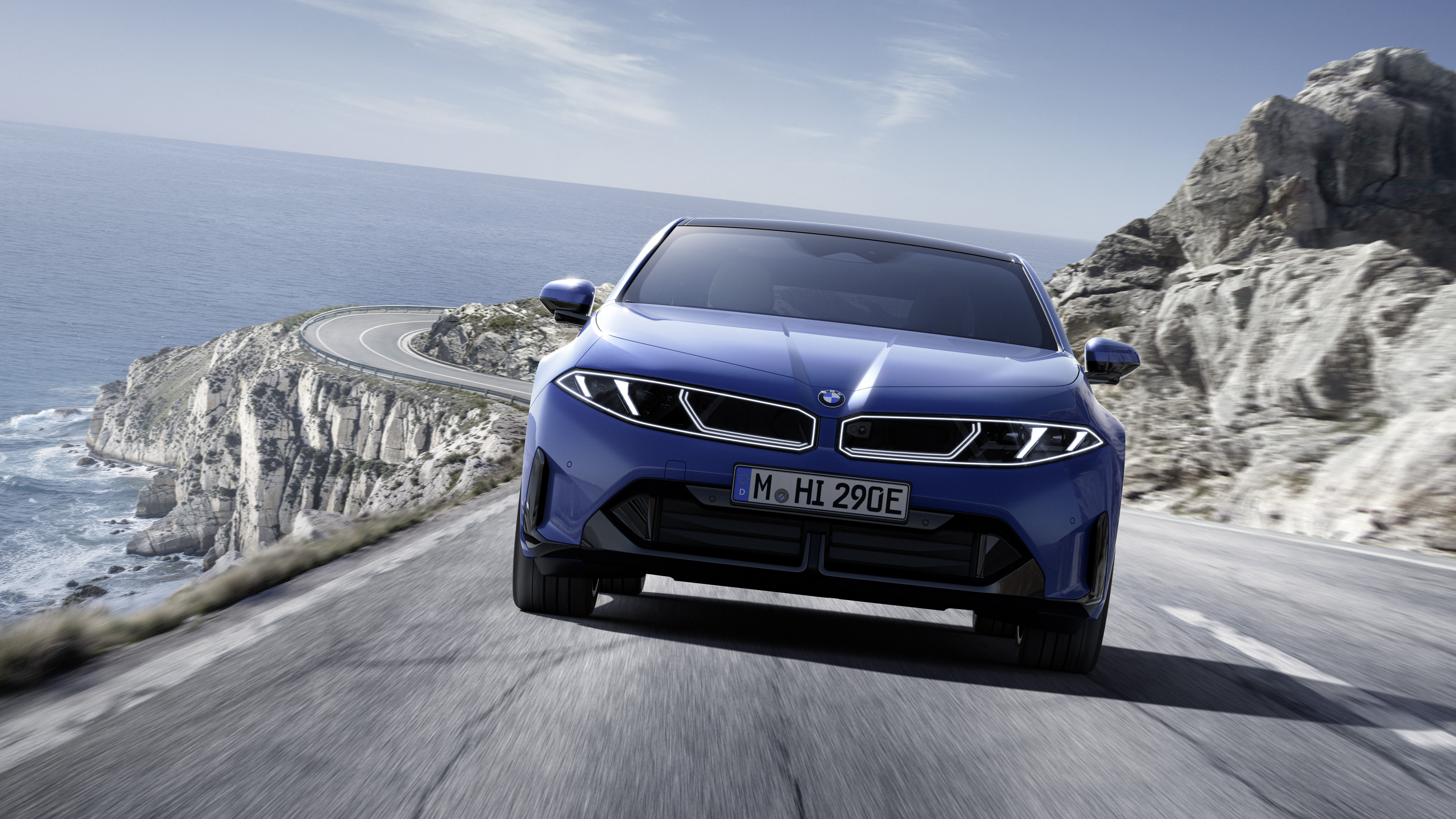 Ein blauer BMW i3 fährt auf einer kurvigen Küstenstraße.