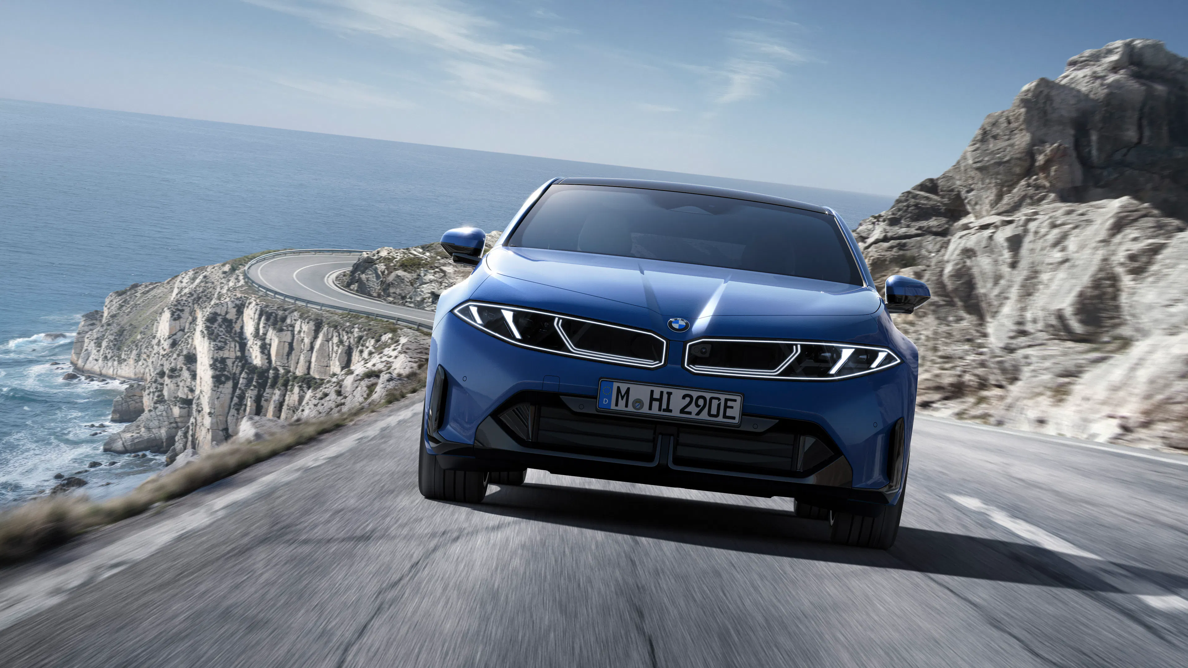 Ein blauer BMW i3 fährt auf einer kurvigen Küstenstraße.