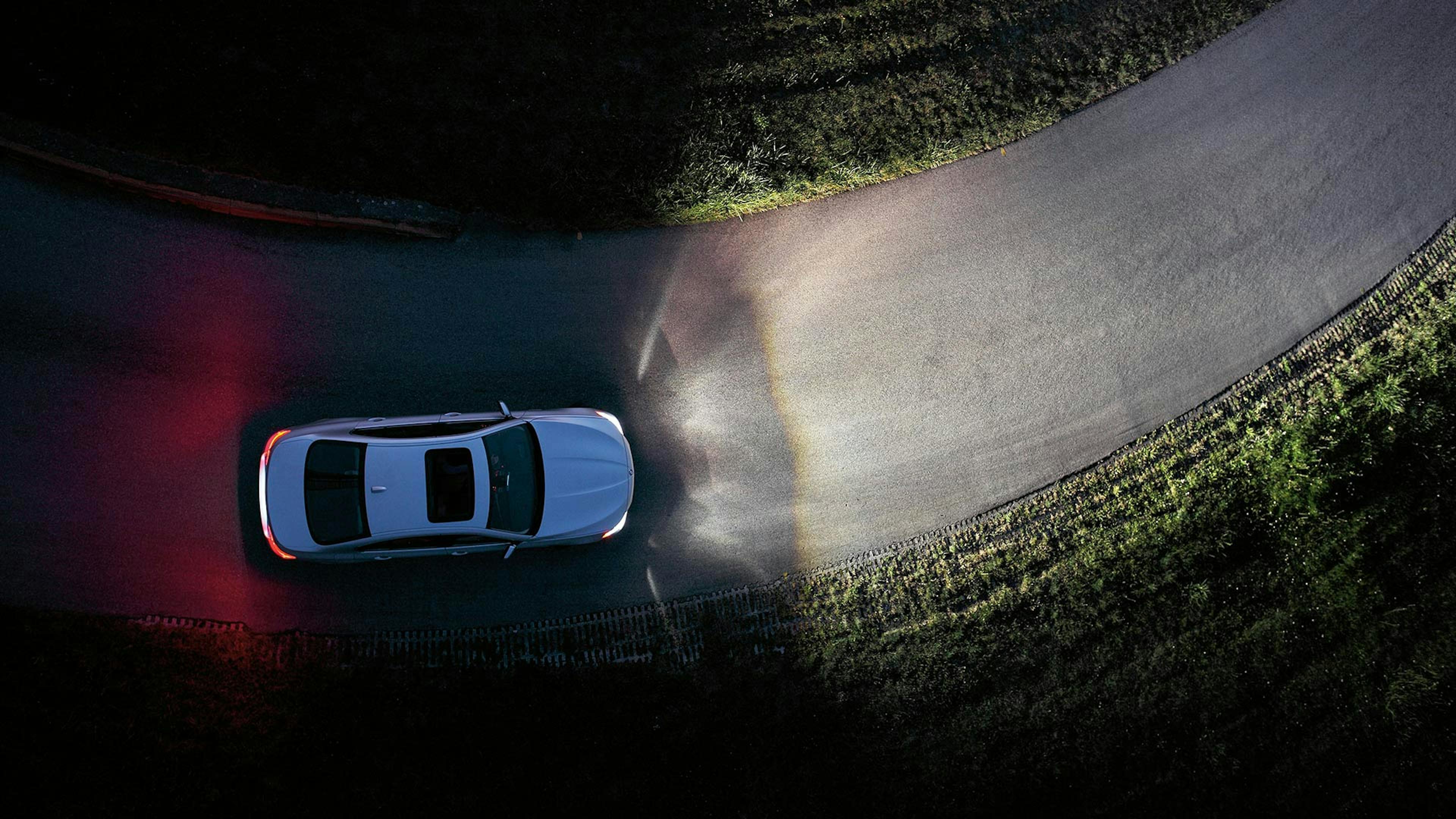 Ein Auto mit eingeschaltetem Kurvenlicht fährt im Dunkeln eine Straße entlang.