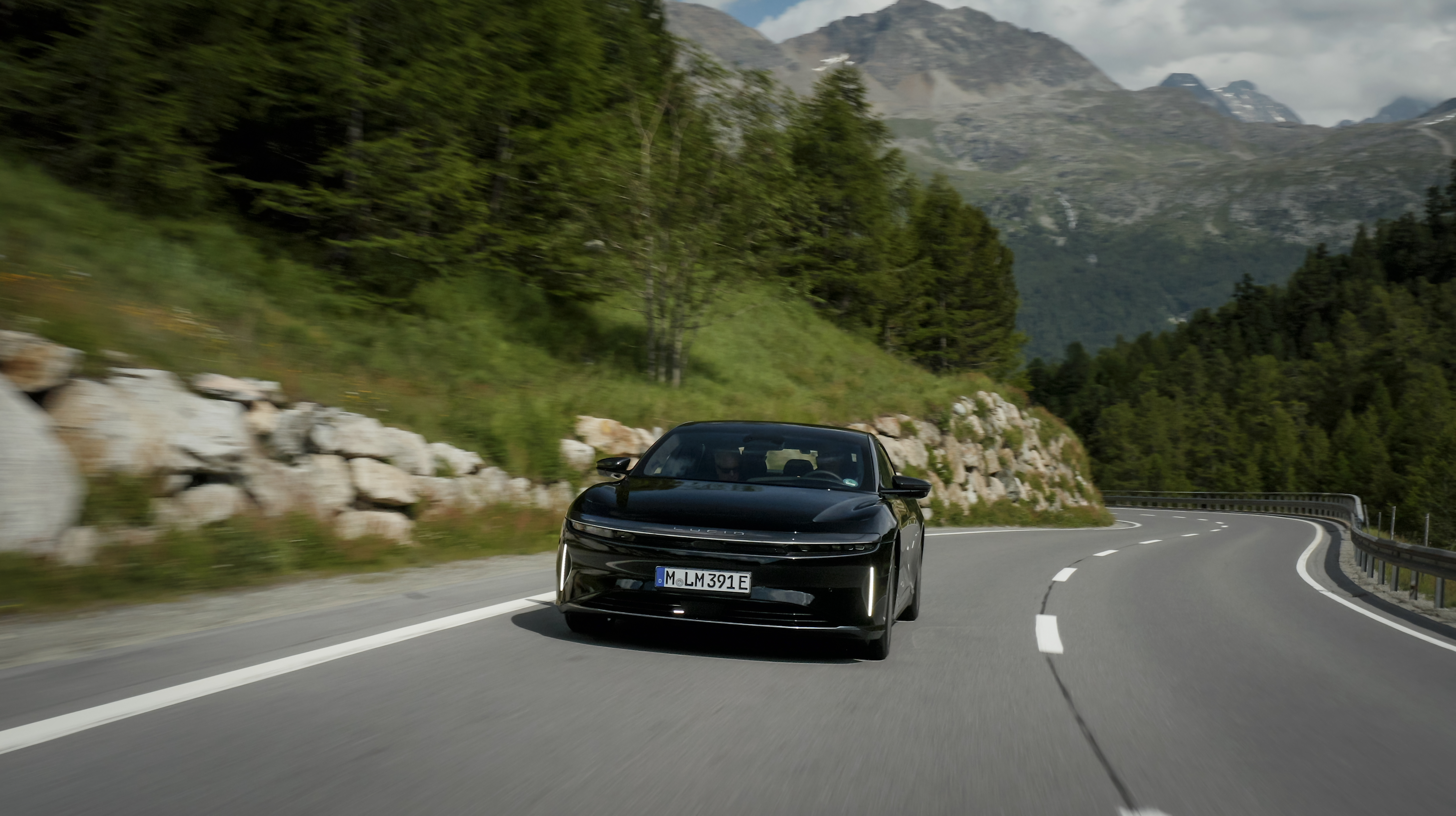 Ein dunkel lackierter Lucid Air Grand Touring fährt eine Bergstraße entlang.
