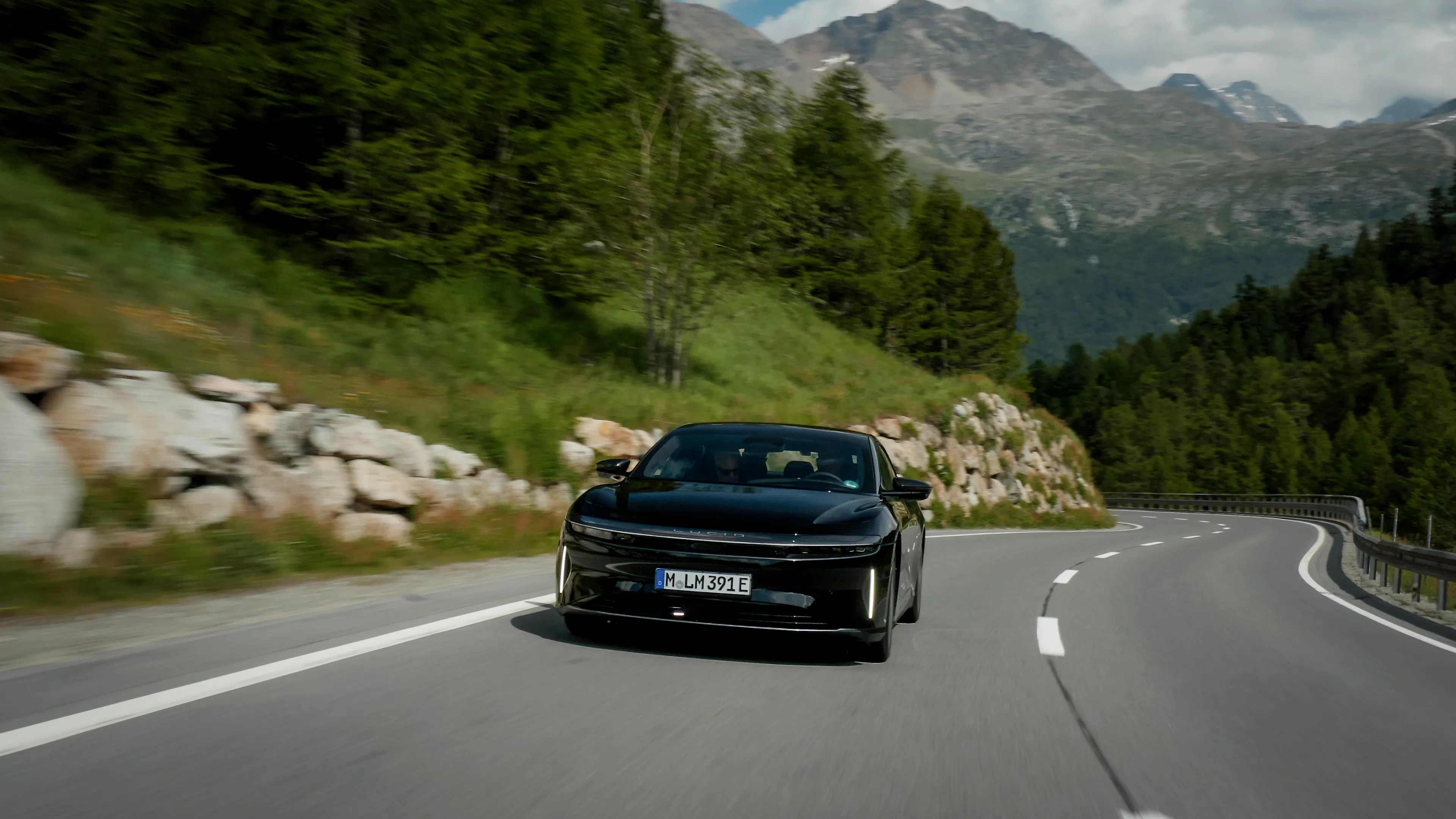 Ein dunkel lackierter Lucid Air Grand Touring fährt eine Bergstraße entlang.