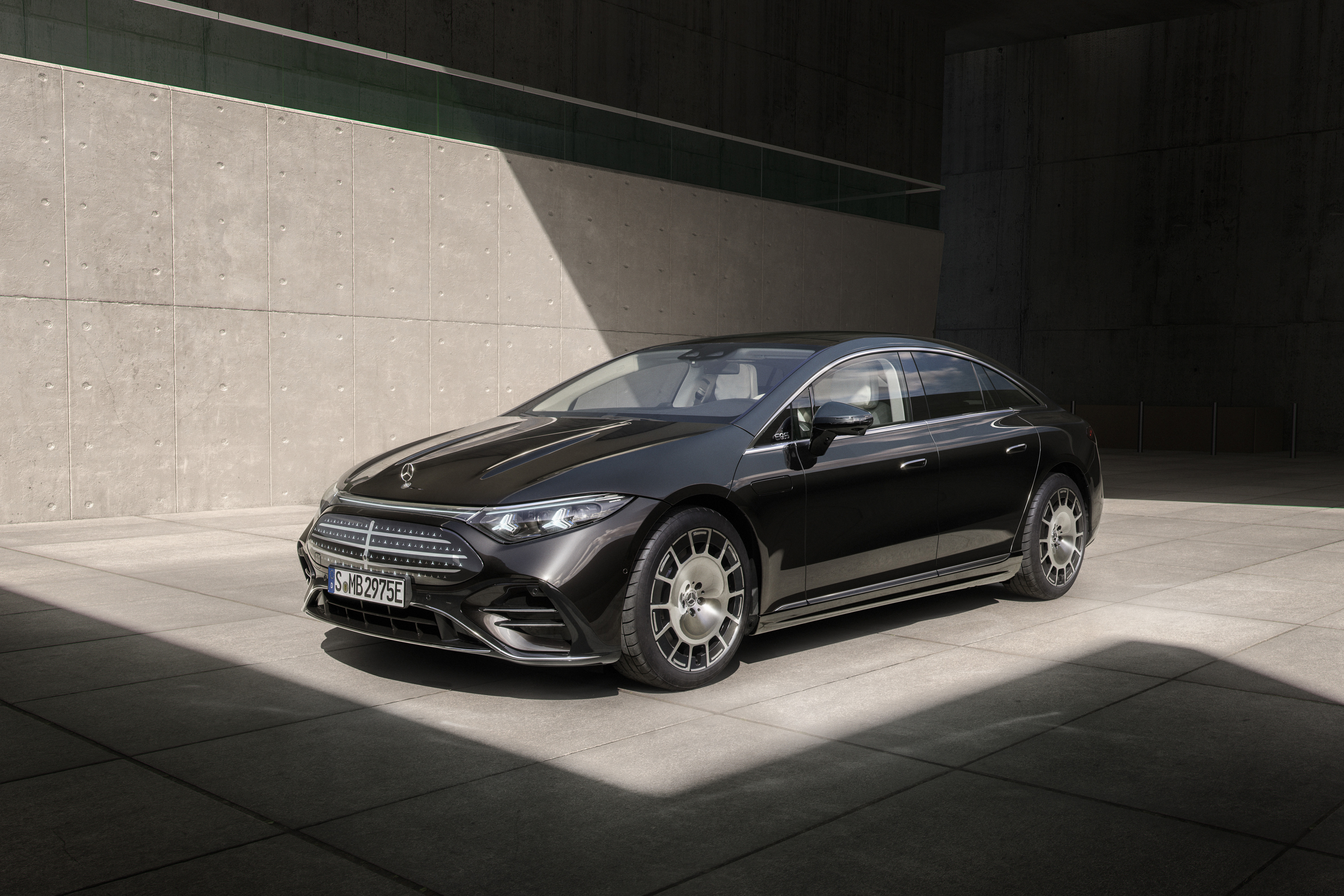 Ein dunkel lackierter Mercedes-Benz EQS 580 4Matic steht vor einer grauen Wand.