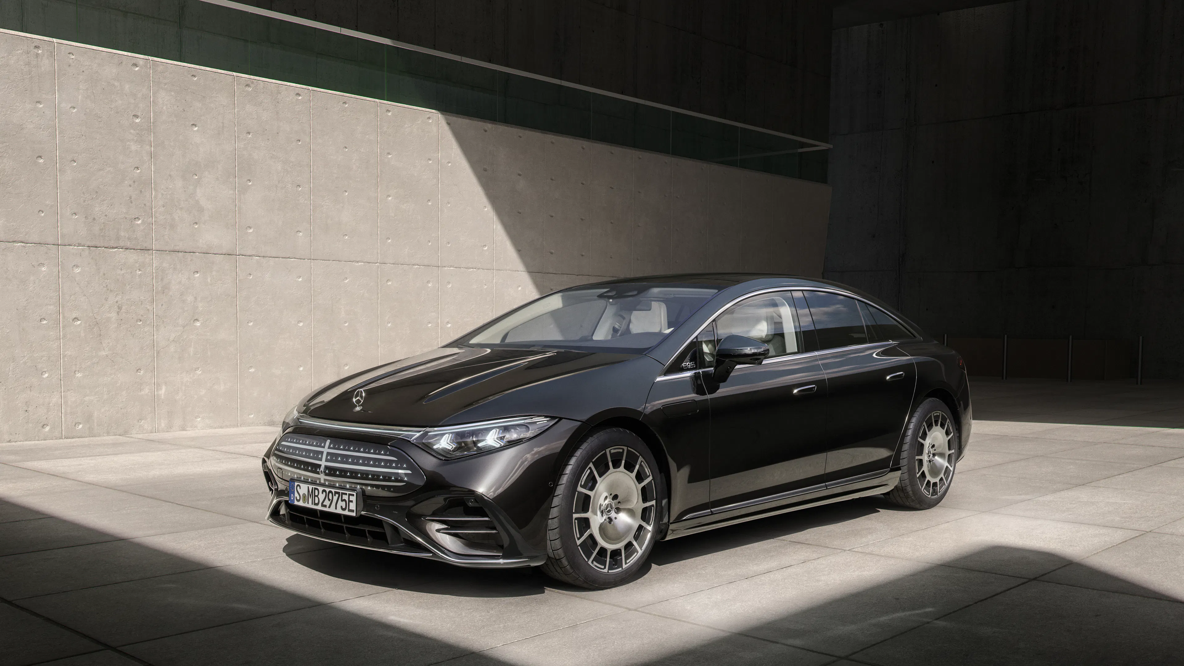 Ein dunkel lackierter Mercedes-Benz EQS 580 4Matic steht vor einer grauen Wand.