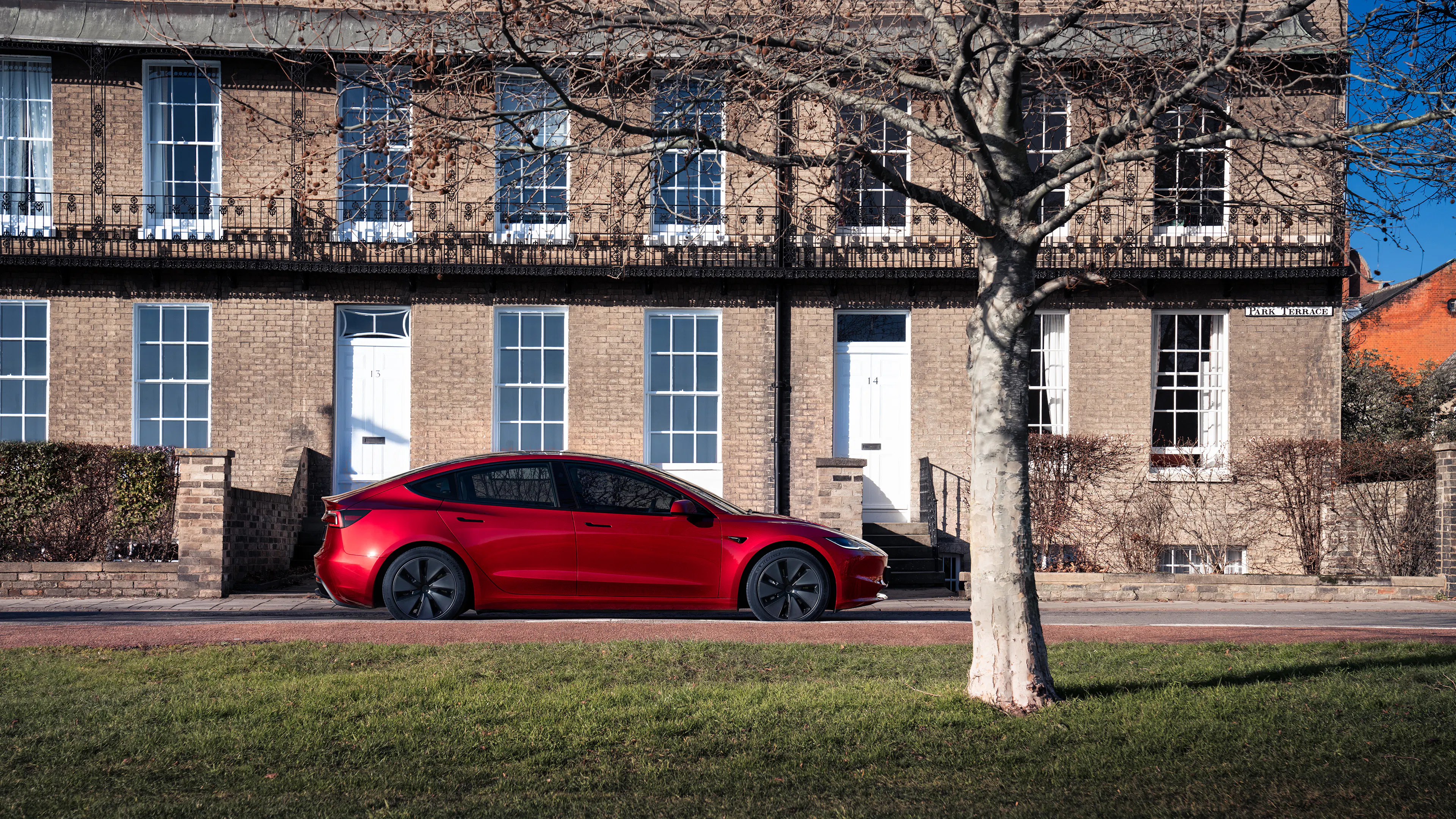 Ein roter Tesla Model 3 fährt an einem Gebäude vorbei.