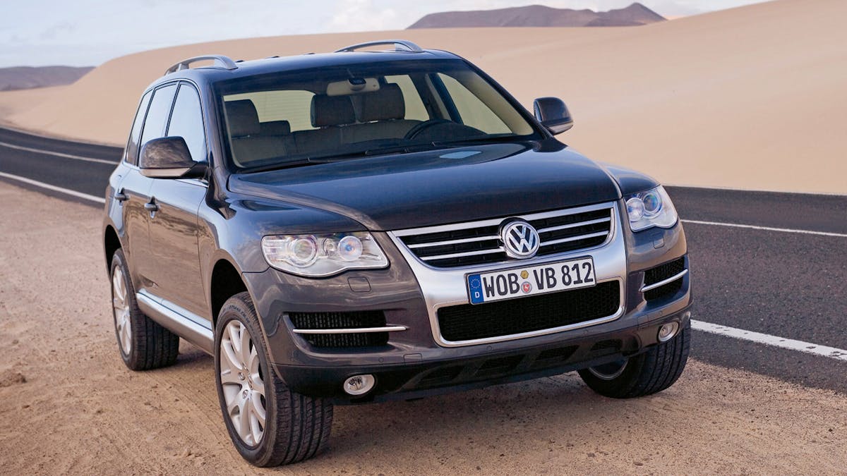 Ein schwarzer VW Touareg Geländewagen steht am Rand einer Straße, die durch eine Wüstenlandschaft führt.