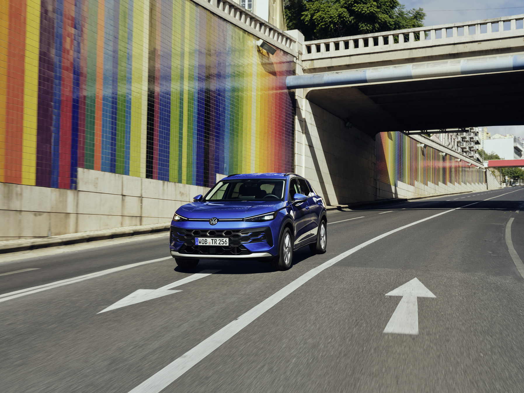 Ein blauer VW T-Roc fährt an einer bunt bemalten Wand vorbei.
