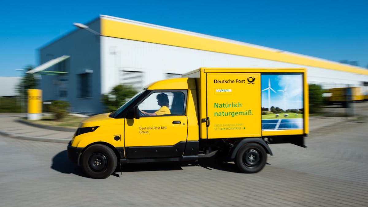 Ein gelber Streetscooter Elektrotransporter der Deutschen Post fährt an einer Lagerhalle vorbei