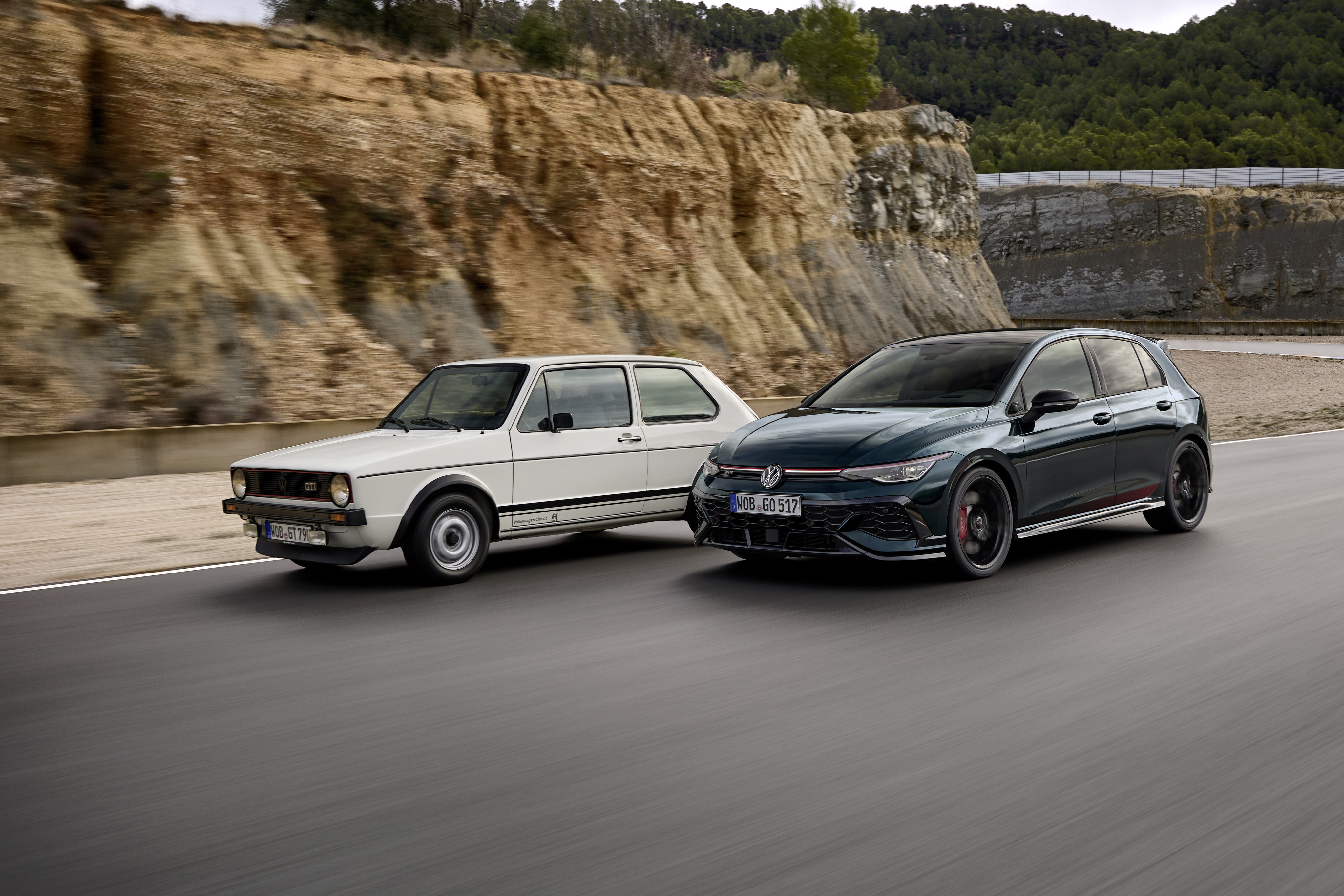 Ein dunkelgrüner VW Golf 8 GTI Edition 50 und ein weißer VW Golf I fahren auf einer Rennstrecke.