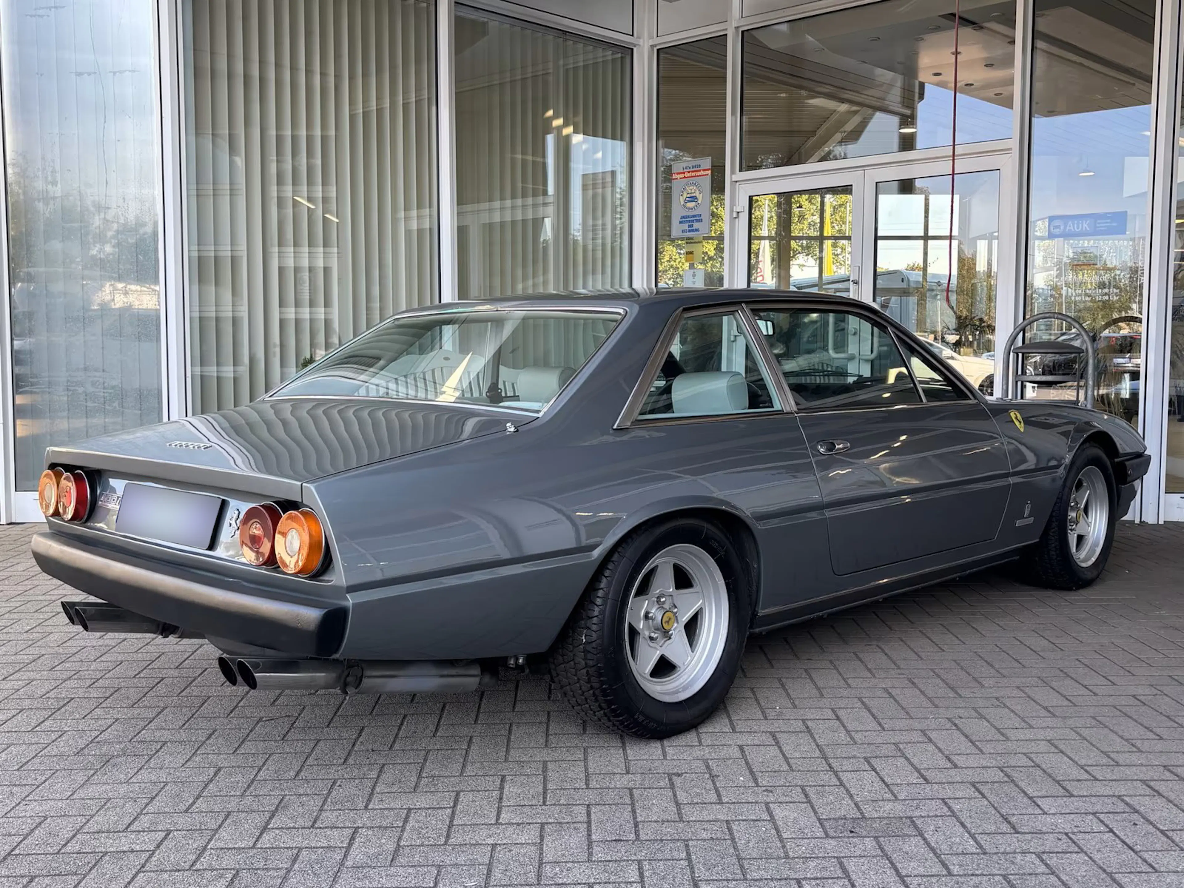 Ein grauer Ferrari 400, der einst dem Formel-1-Fahrer Jody Scheckter gehörte, steht auf einer gepflasterten Fläche.