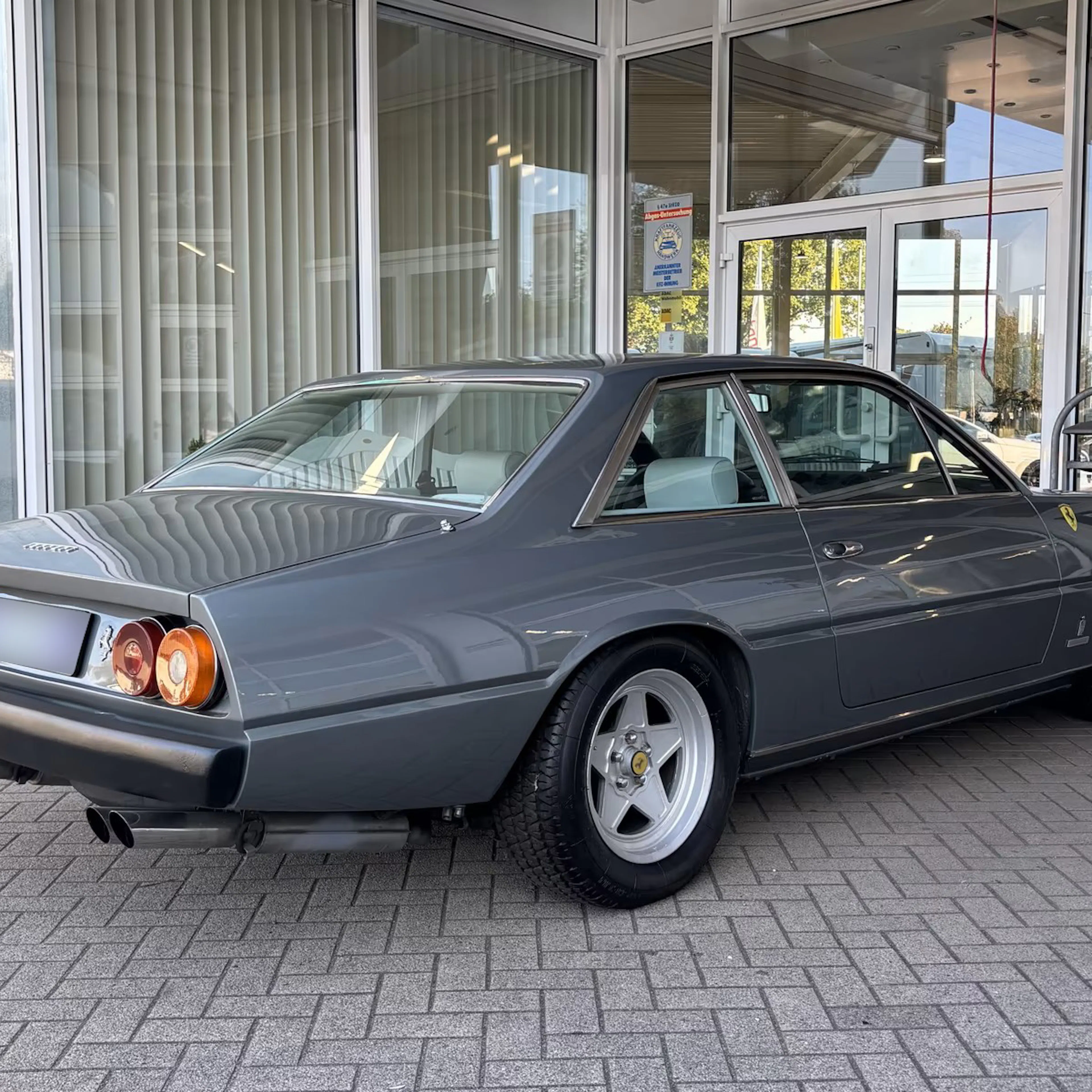 Ein grauer Ferrari 400, der einst dem Formel-1-Fahrer Jody Scheckter gehörte, steht auf einer gepflasterten Fläche.