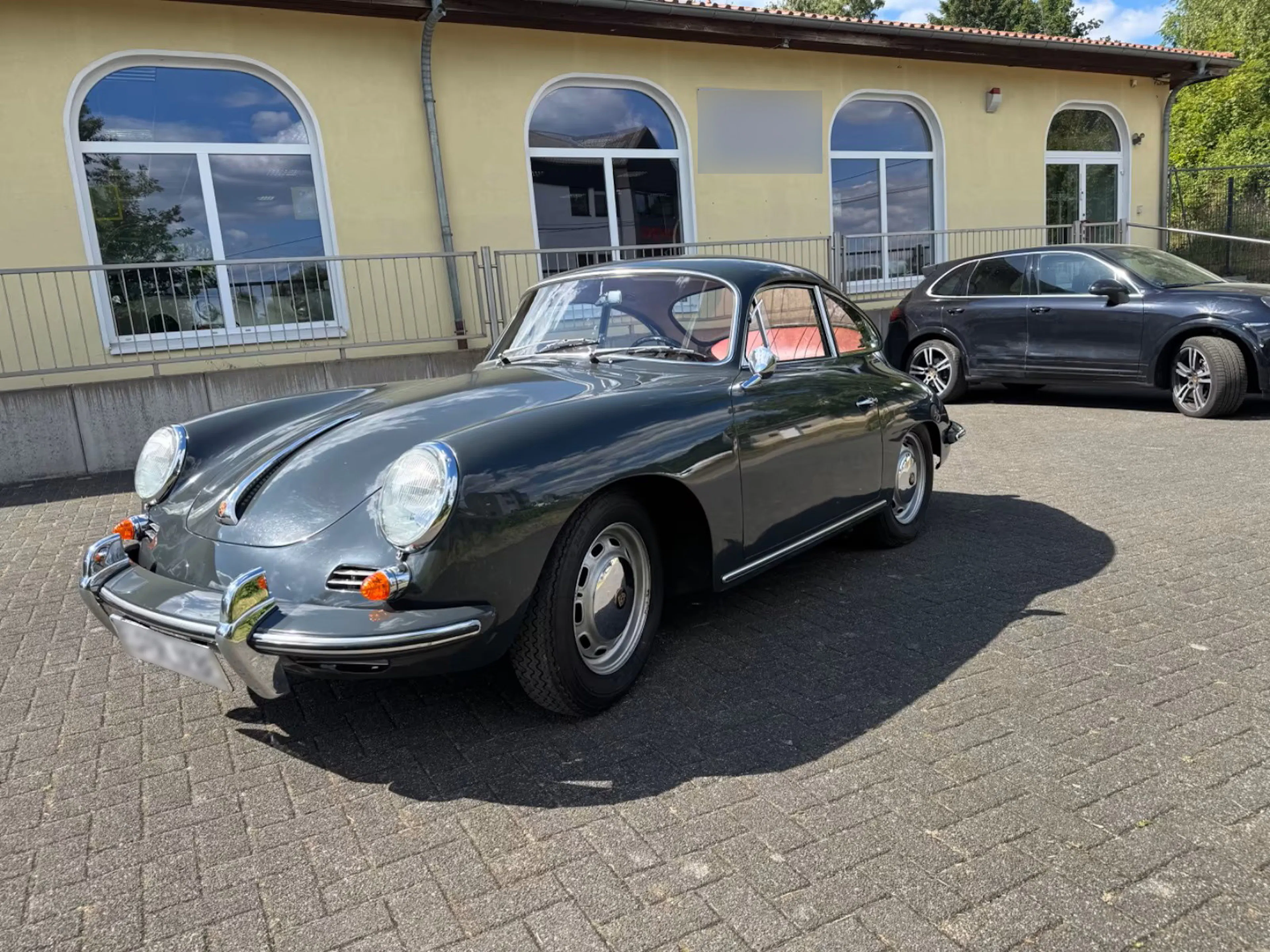 Ein grauer Porsche 356, der einst dem Fußballprofi Paul Breitner gehörte, steht auf einer gepflasterten Fläche.
