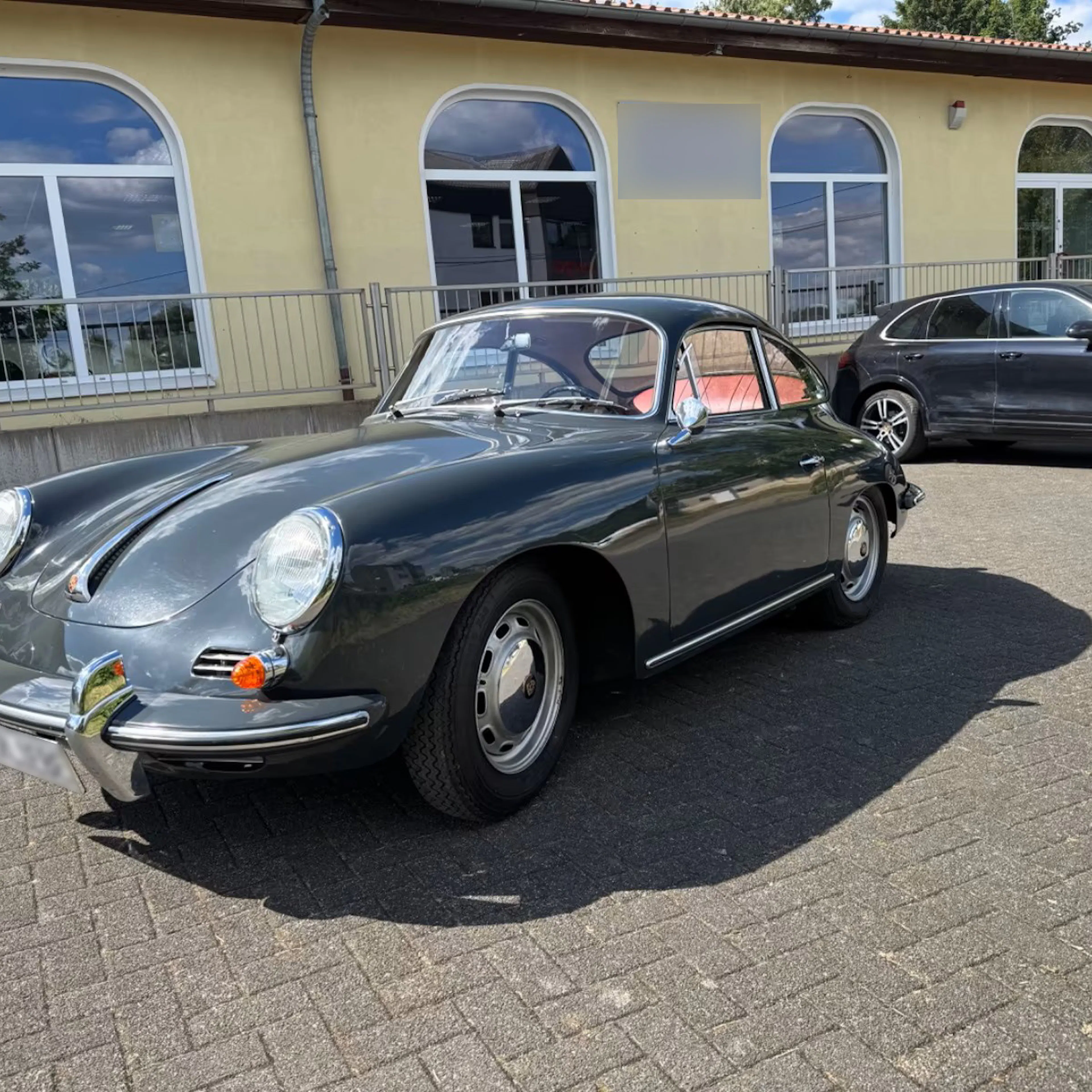 Ein grauer Porsche 356, der einst dem Fußballprofi Paul Breitner gehörte, steht auf einer gepflasterten Fläche.