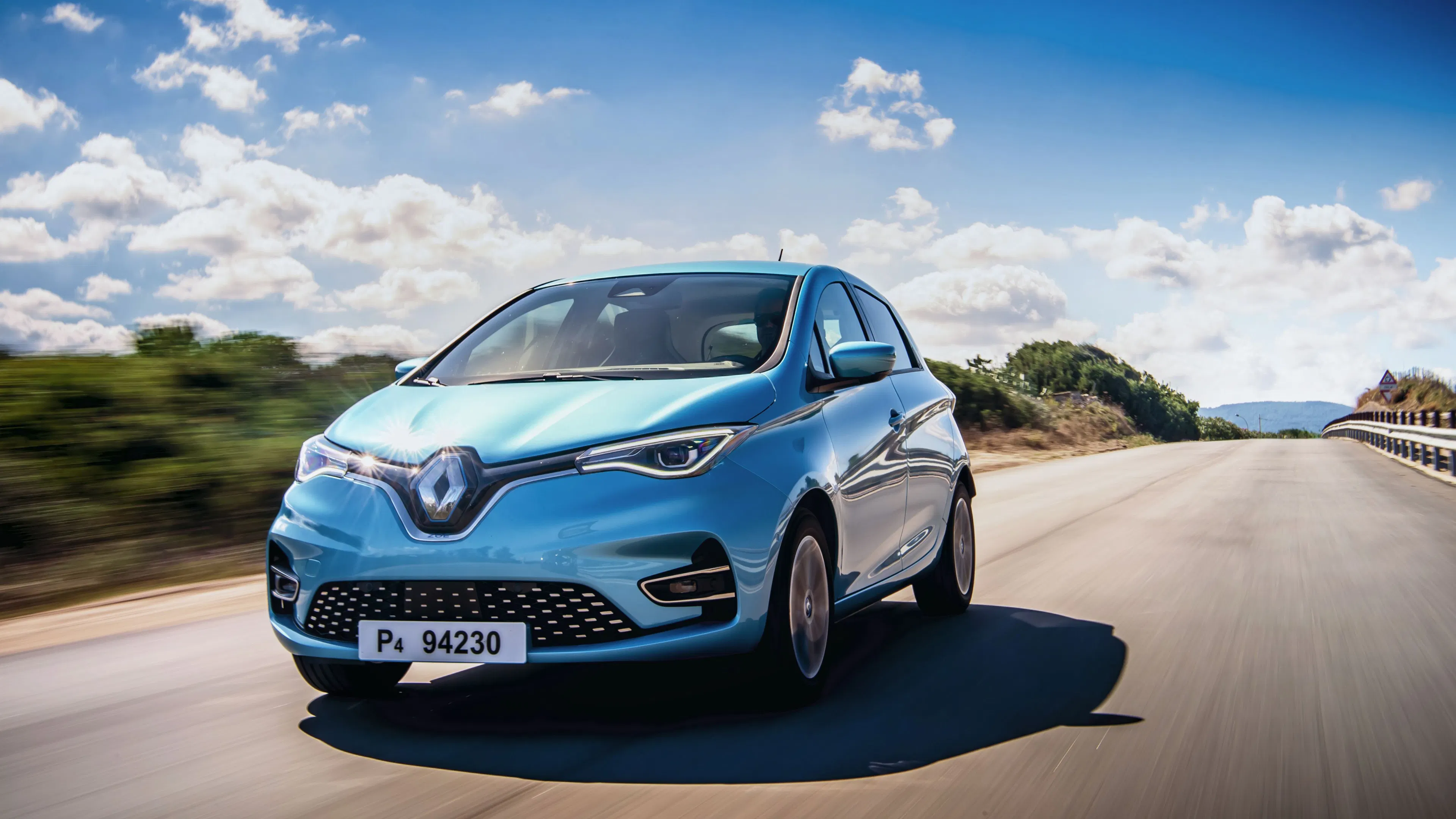 Ein hellblauer Renault Zoe fährt auf einer mediterranen Landstraße.