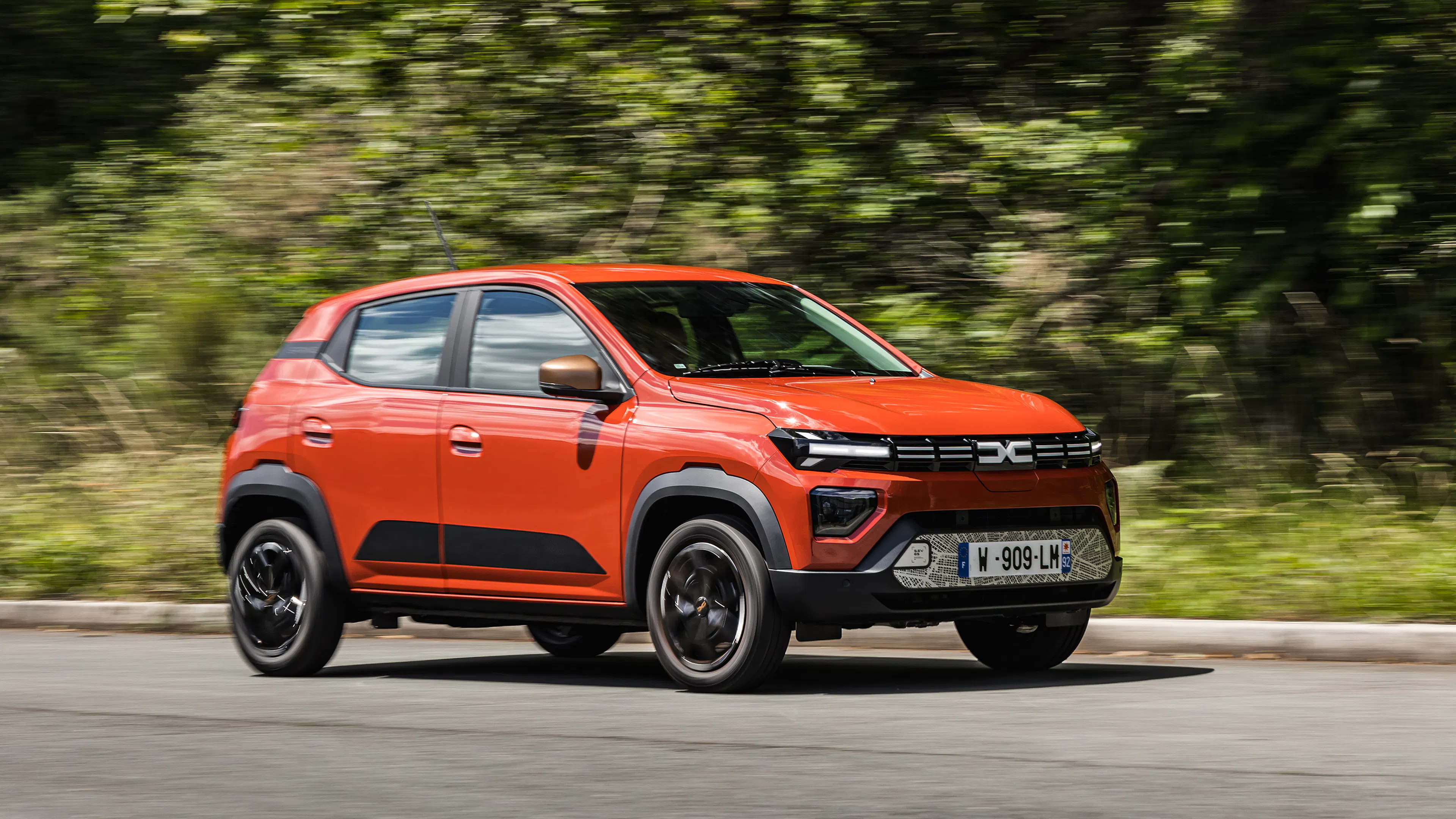 Ein roter Dacia Spring Electric fährt auf einer Landstraße.