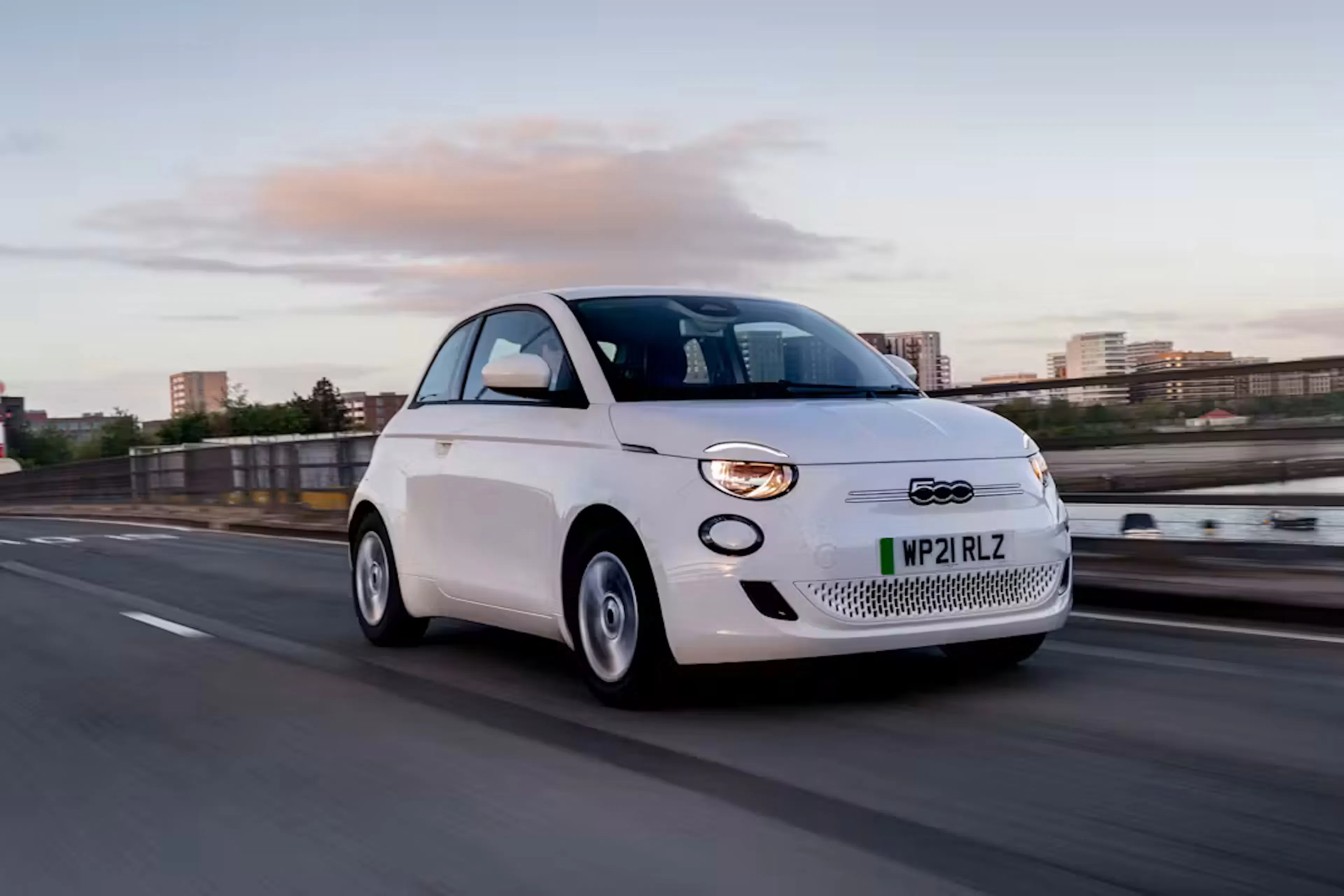 Ein weißer Fiat 500e fährt in einer Stadt.
