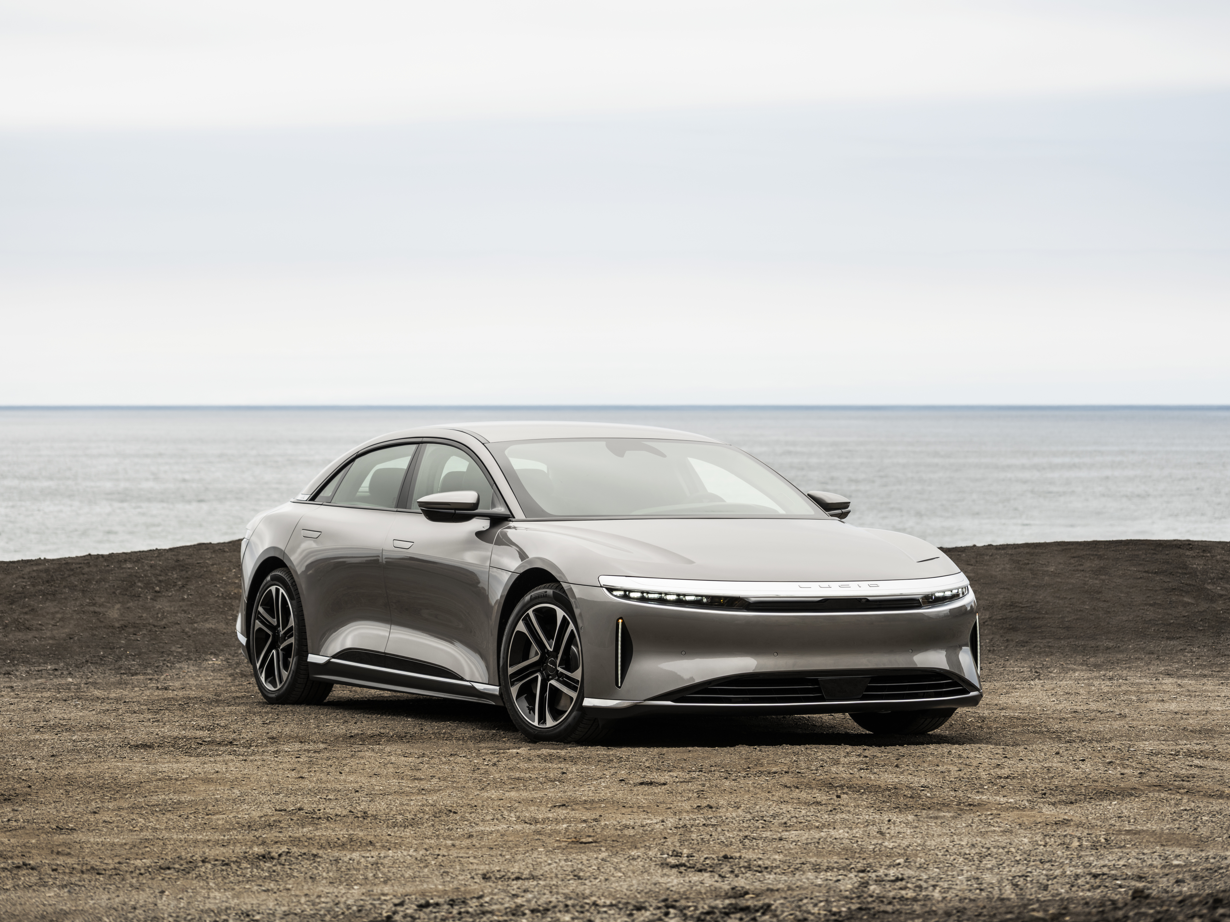 Ein silberner Lucid Air steht auf einer Wiese vor einem Meer.