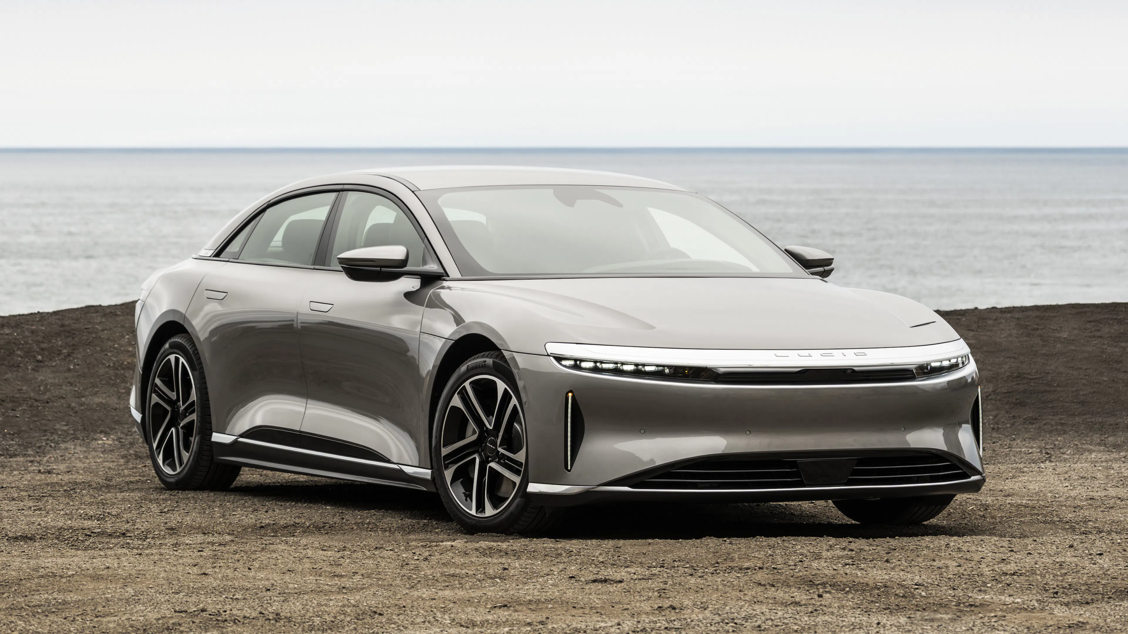 Ein silberner Lucid Air steht auf einer Wiese vor einem Meer.