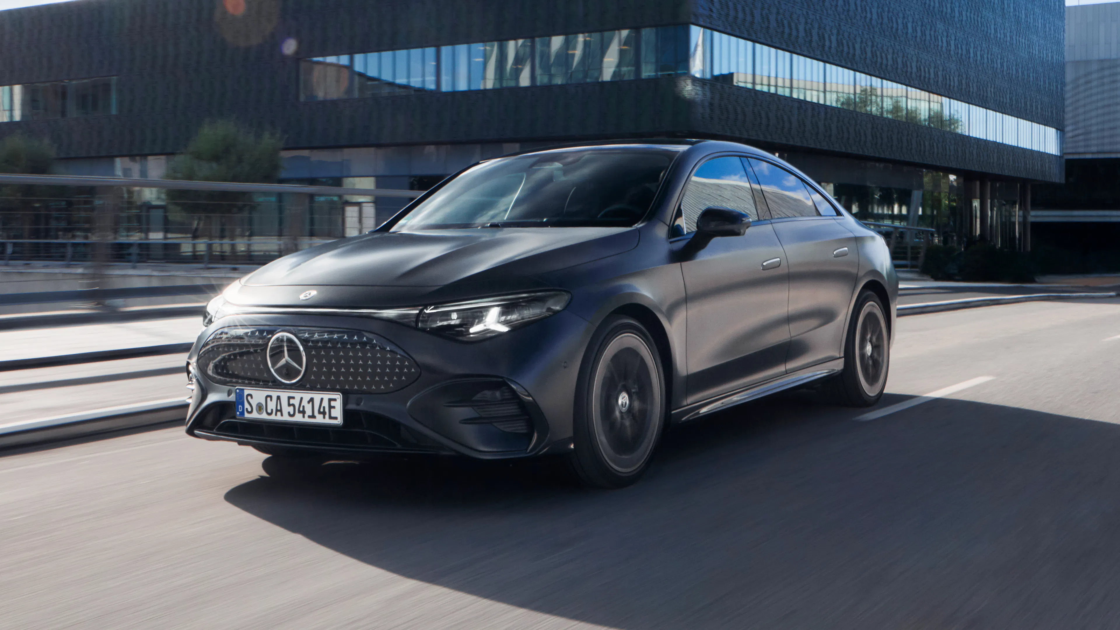 Ein schwarzes Mercedes-Benz CLA Coupé 250 EQ fährt an einem schwarzen Gebäude in einer Stadt vorbei.