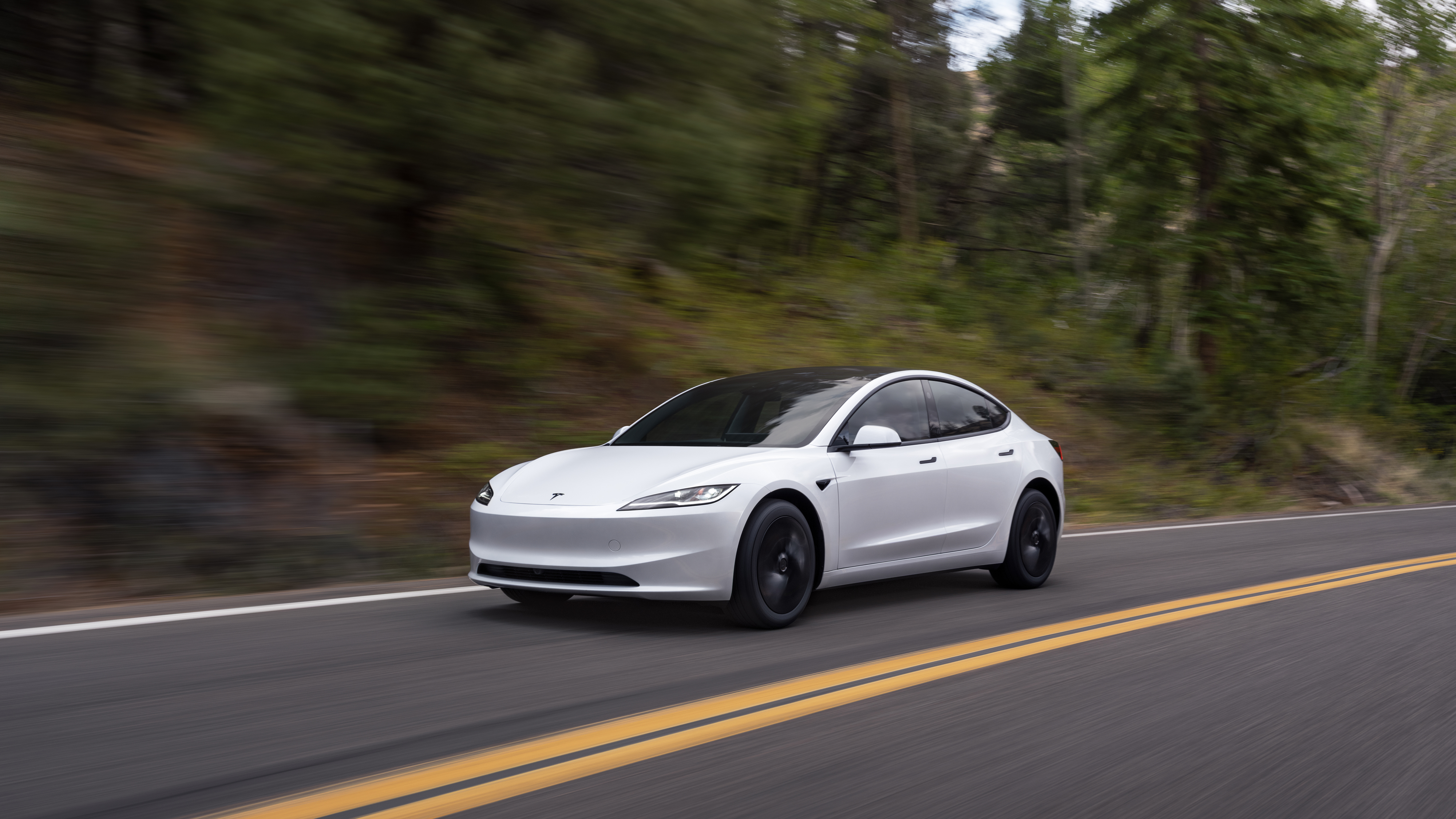 Ein weißer Tesla Model 3 fährt auf einer Landstraße in den USA.