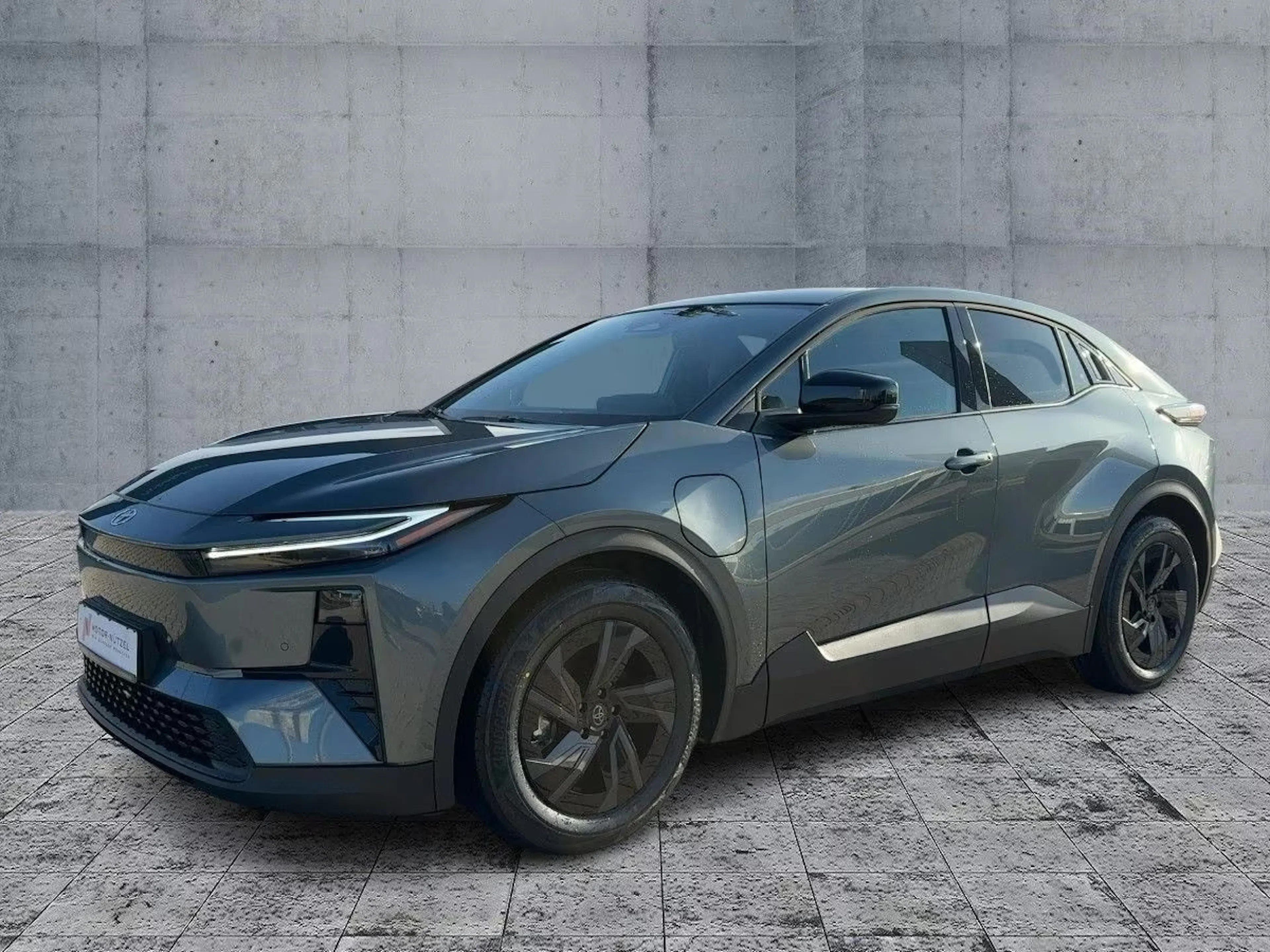 Ein dunkelgrauer Toyota C-HR+ steht auf einem gepflasterten Platz.