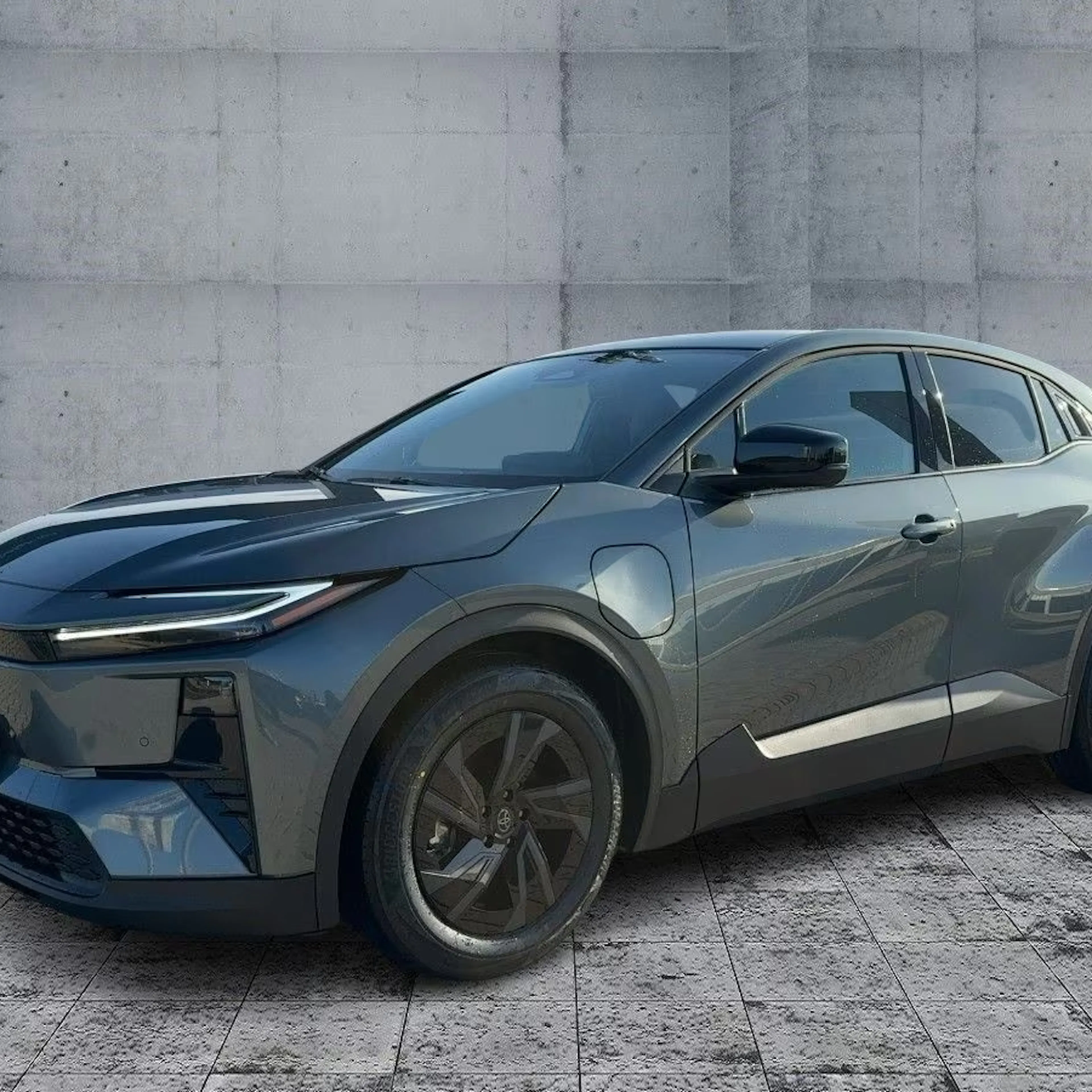 Ein dunkelgrauer Toyota C-HR+ steht auf einem gepflasterten Platz.