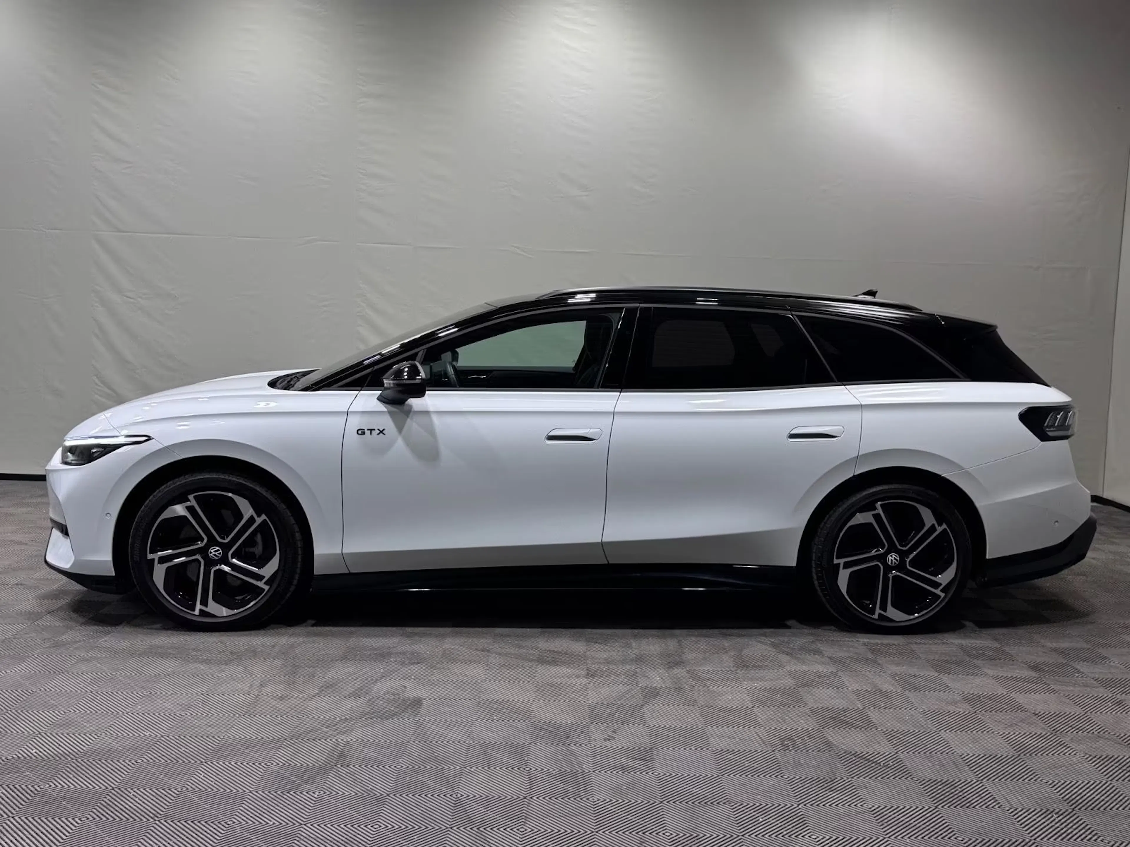 Ein weißer VW ID.7 GTX Tourer steht vor einer grauen Wand.