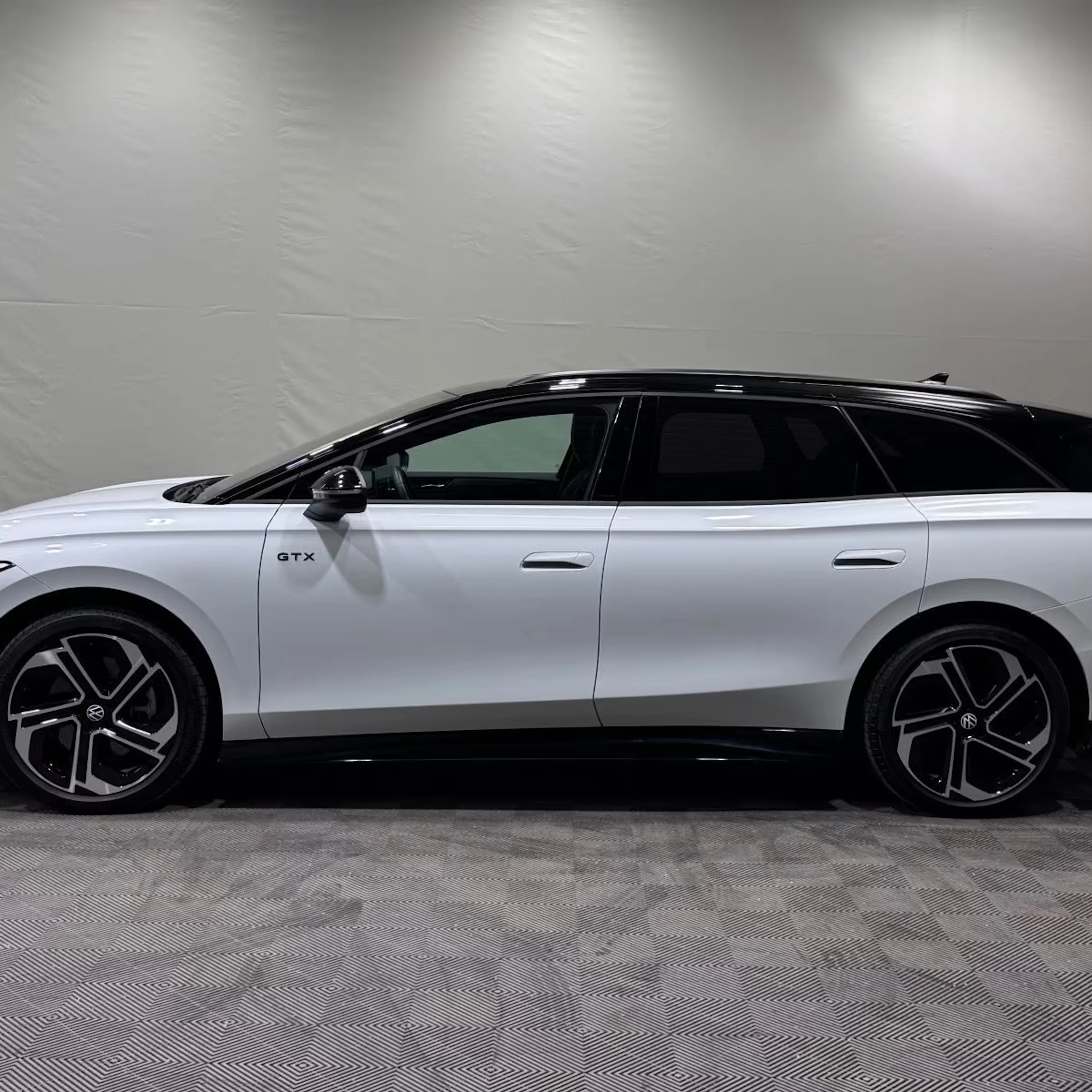 Ein weißer VW ID.7 GTX Tourer steht vor einer grauen Wand.