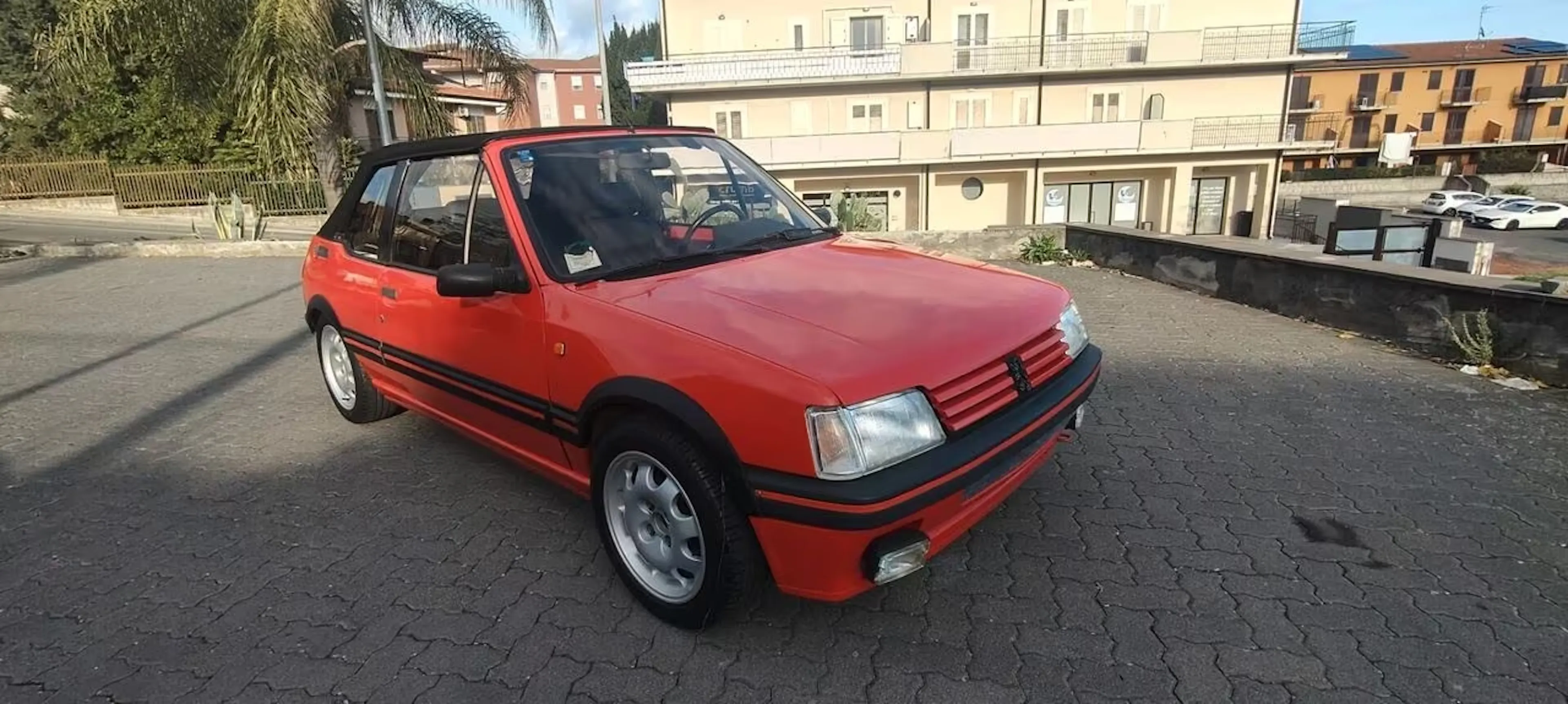Ein roter Peugeot 205 CTI steht in einer Stadt.