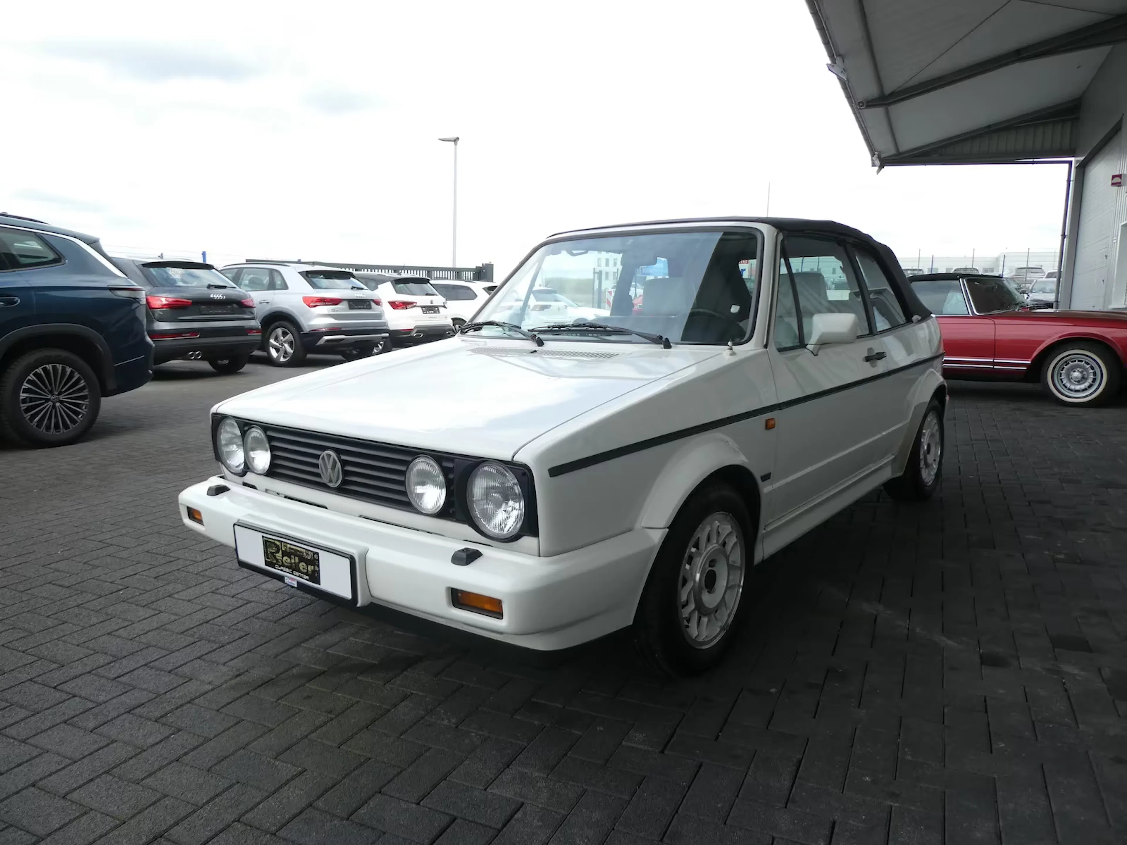 Ein weißes VW Golf I Cabrio steht auf einem Händlerparkplatz