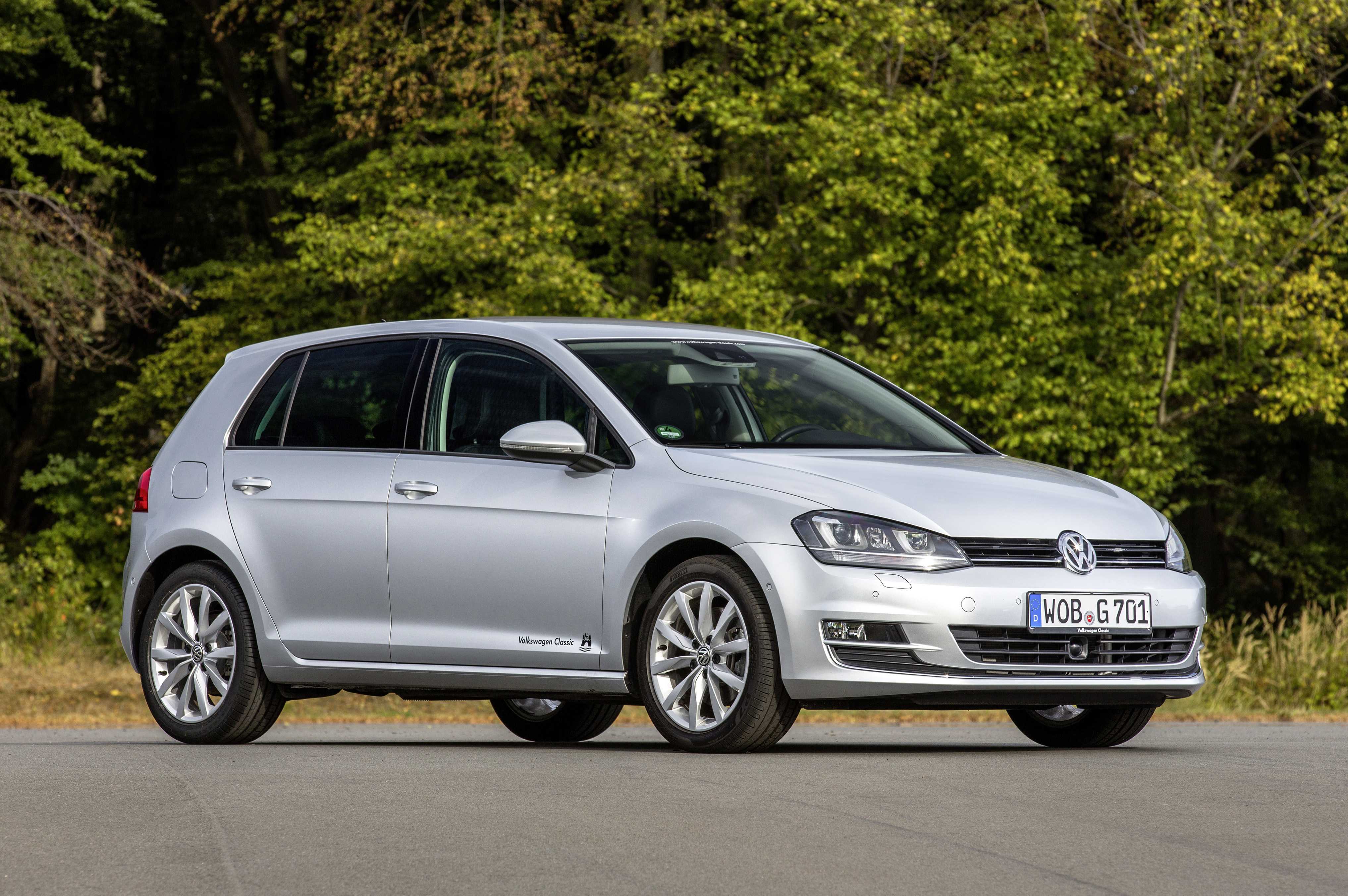Ein silberner VW Golf steht auf einer Straße vor Bäumen.