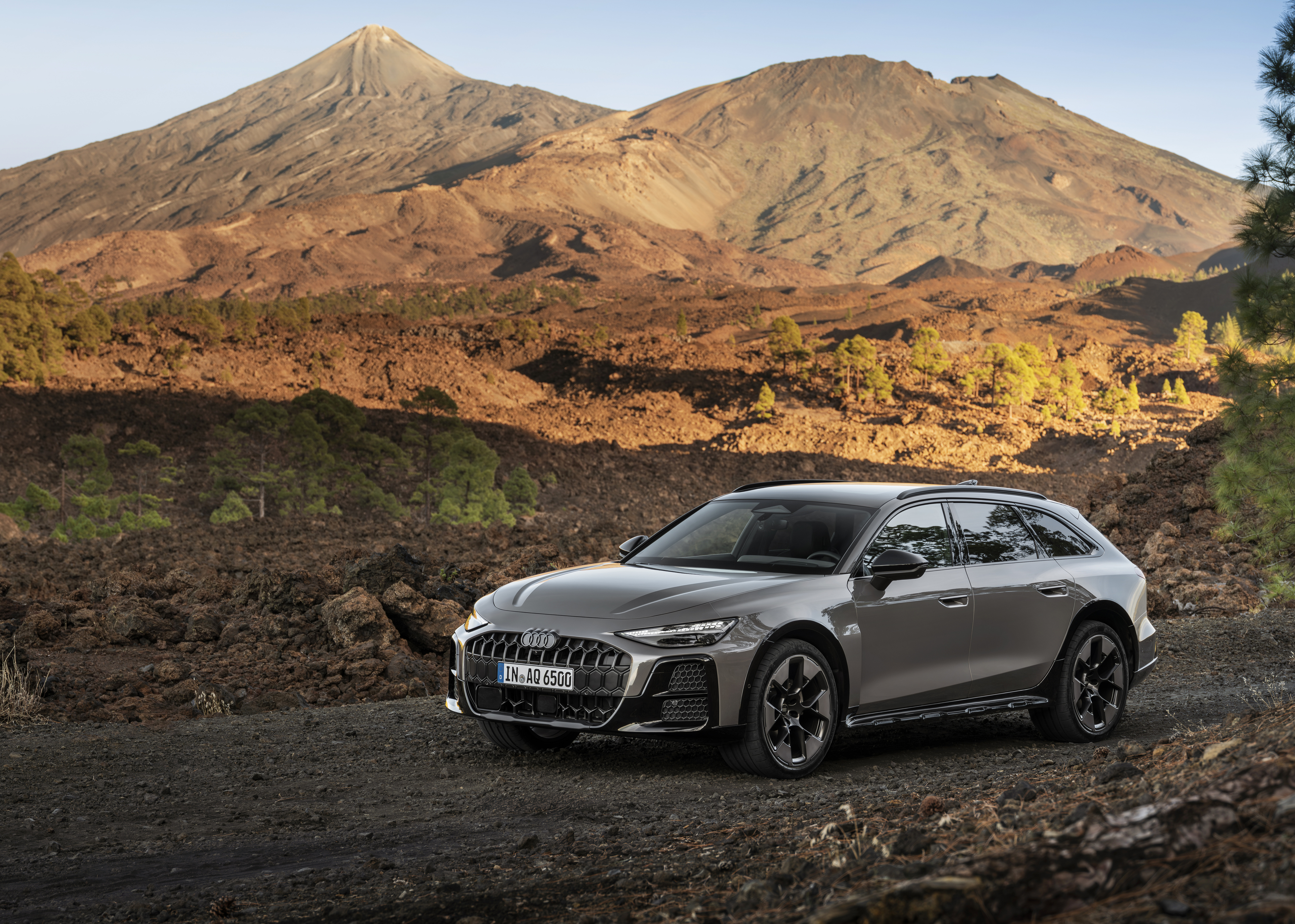 Schrägansicht auf die Front eines dunkelgrauen Audi A6 Allroad, der auf einem Schotterweg in einer bergigen Landschaft steht.