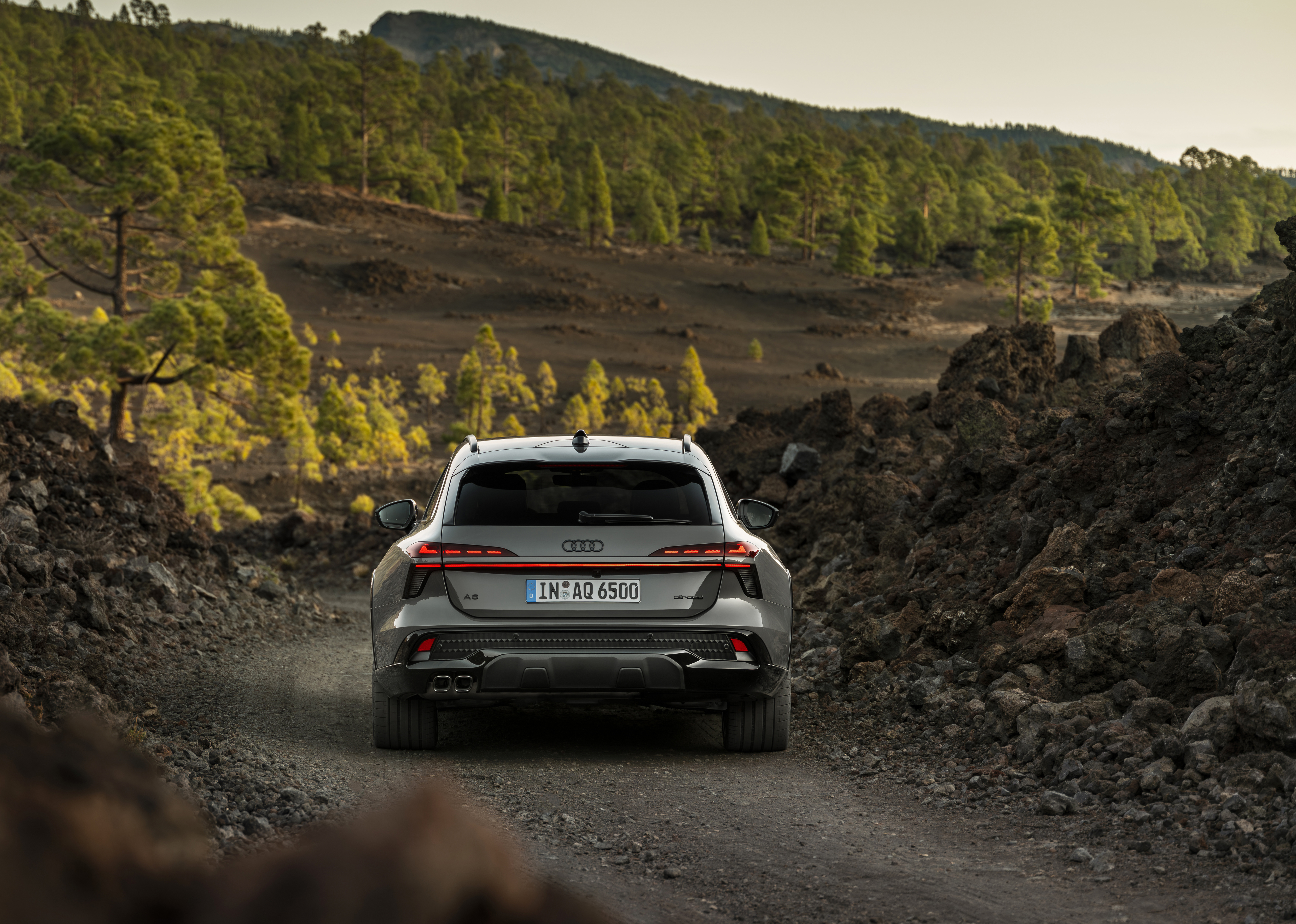 Heckansicht eines dunkelgrauen Audi A6 Allroad, der auf einem Schotterweg in einer bergigen Landschaft steht.