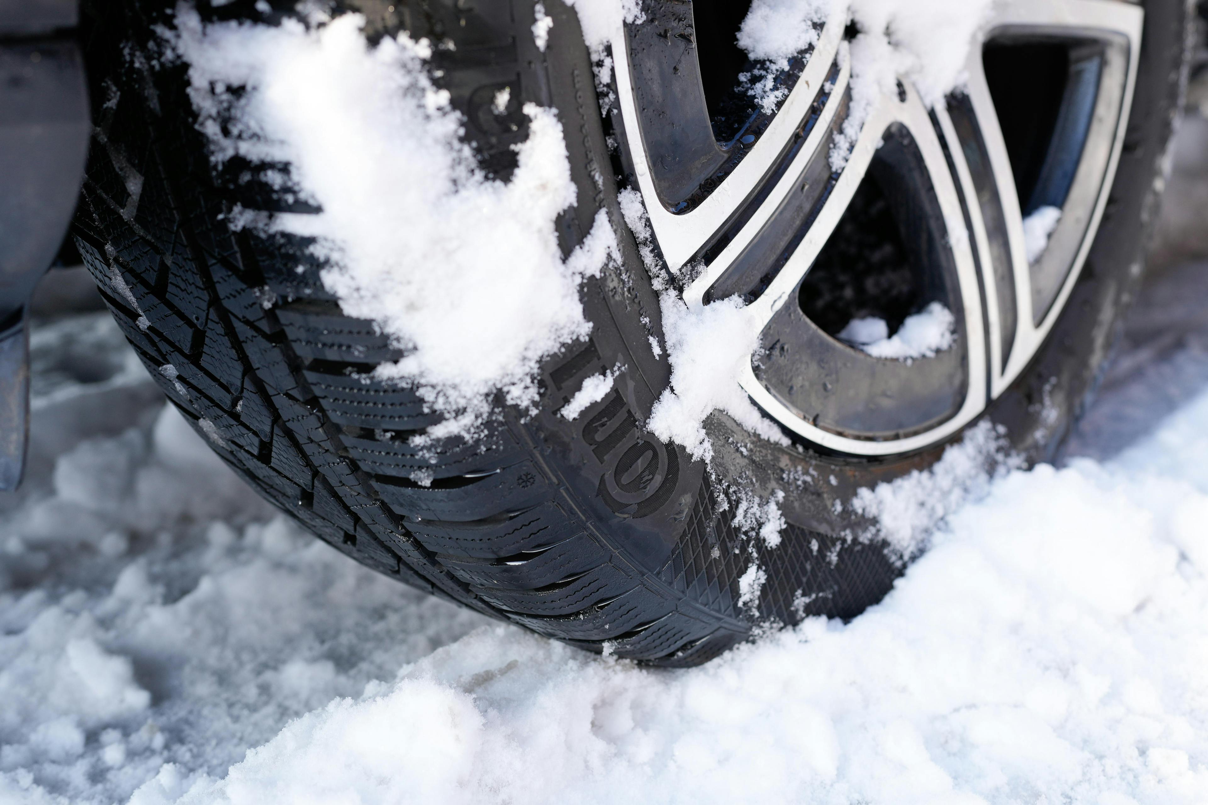 Autoreifen mit Winterprofil fährt durch Schnee, Schnee haftet am Profil.