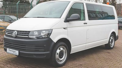 Ein weißer VW ABT e-T6 steht auf einem Parkplatz vor einem Zaun