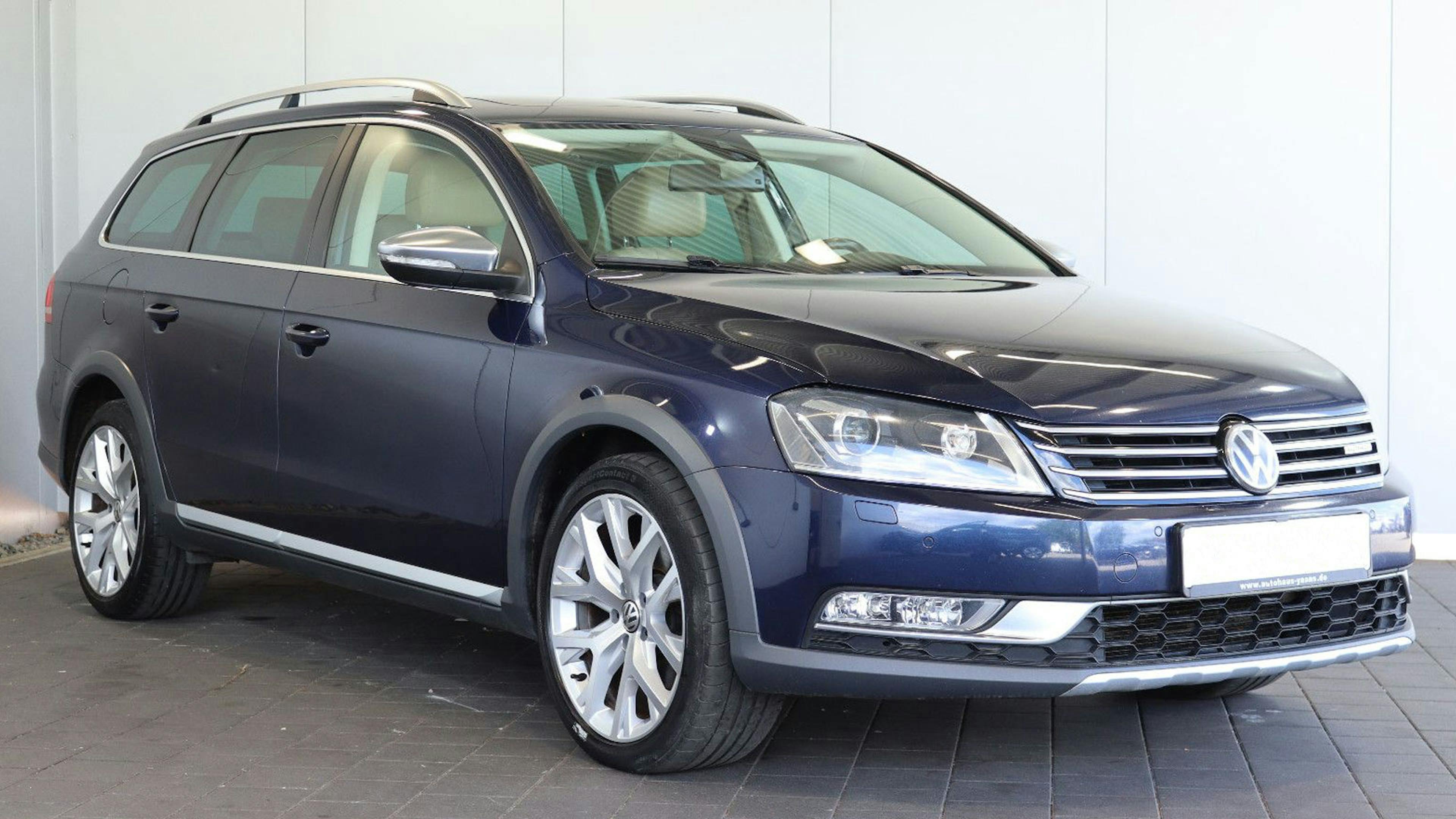 Ein blauer VW Passat B7 Alltrack Kombi steht vor einer weißen Wand.