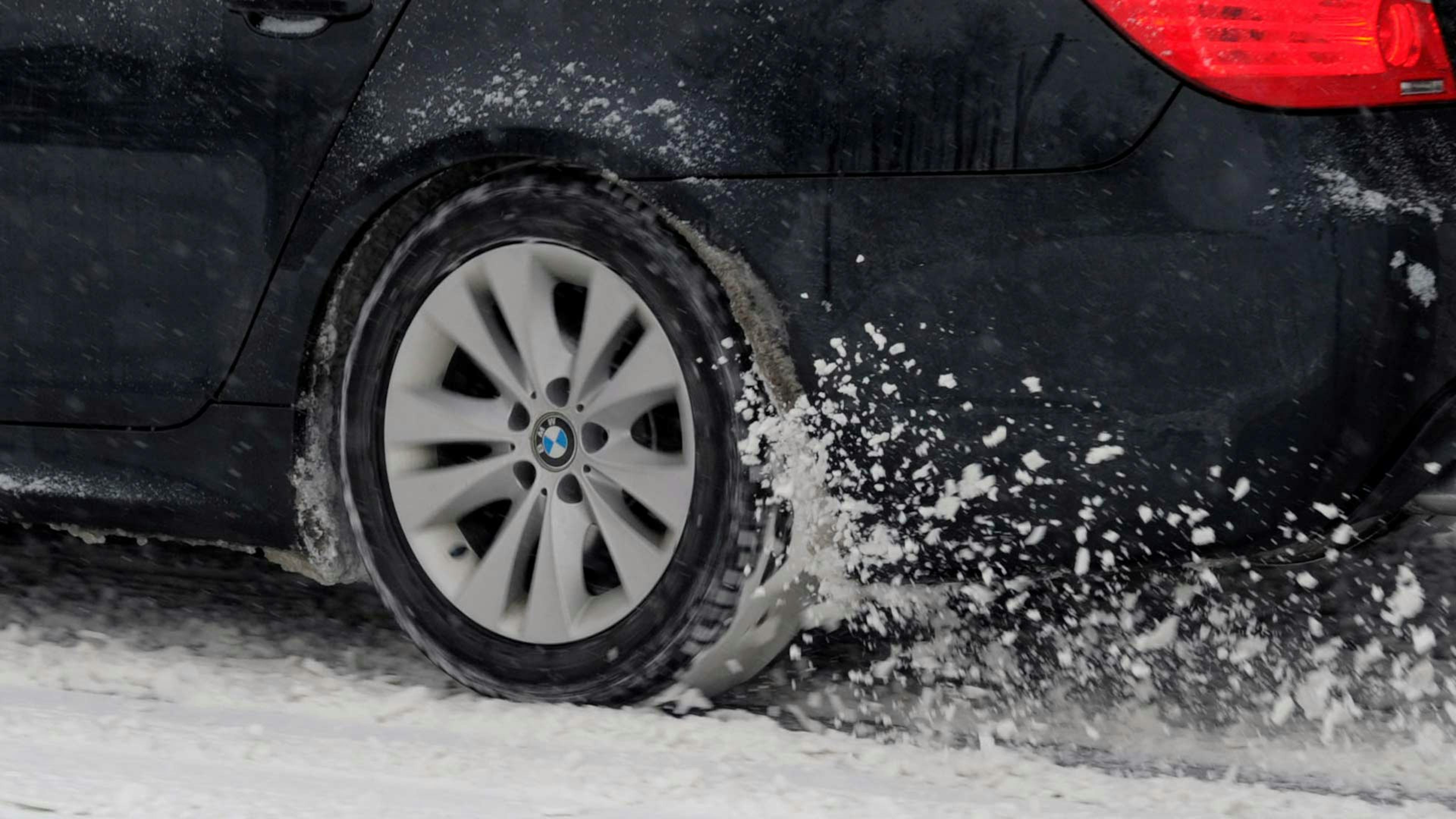 Der Reifen eines BMW mit Heckantrieb dreht auf einer schneebedeckten Straße durch.