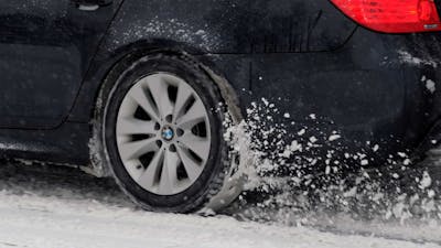 Der Reifen eines BMW mit Heckantrieb dreht auf einer schneebedeckten Straße durch.