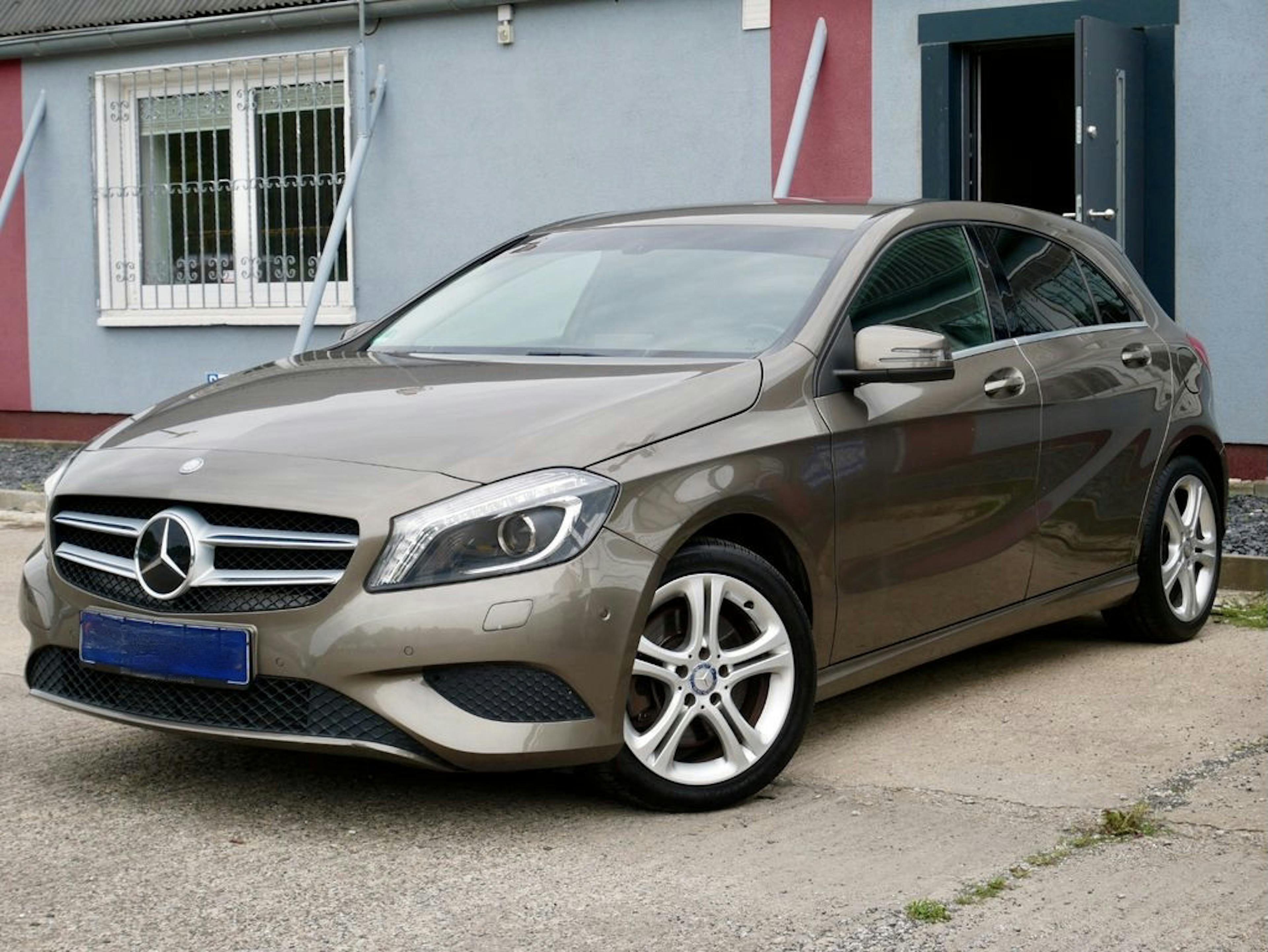 Beiger Mercedes-Benz Kompaktwagen steht auf einem Betonboden vor einem Gebäude mit vergittertem Fenster und offener Tür.