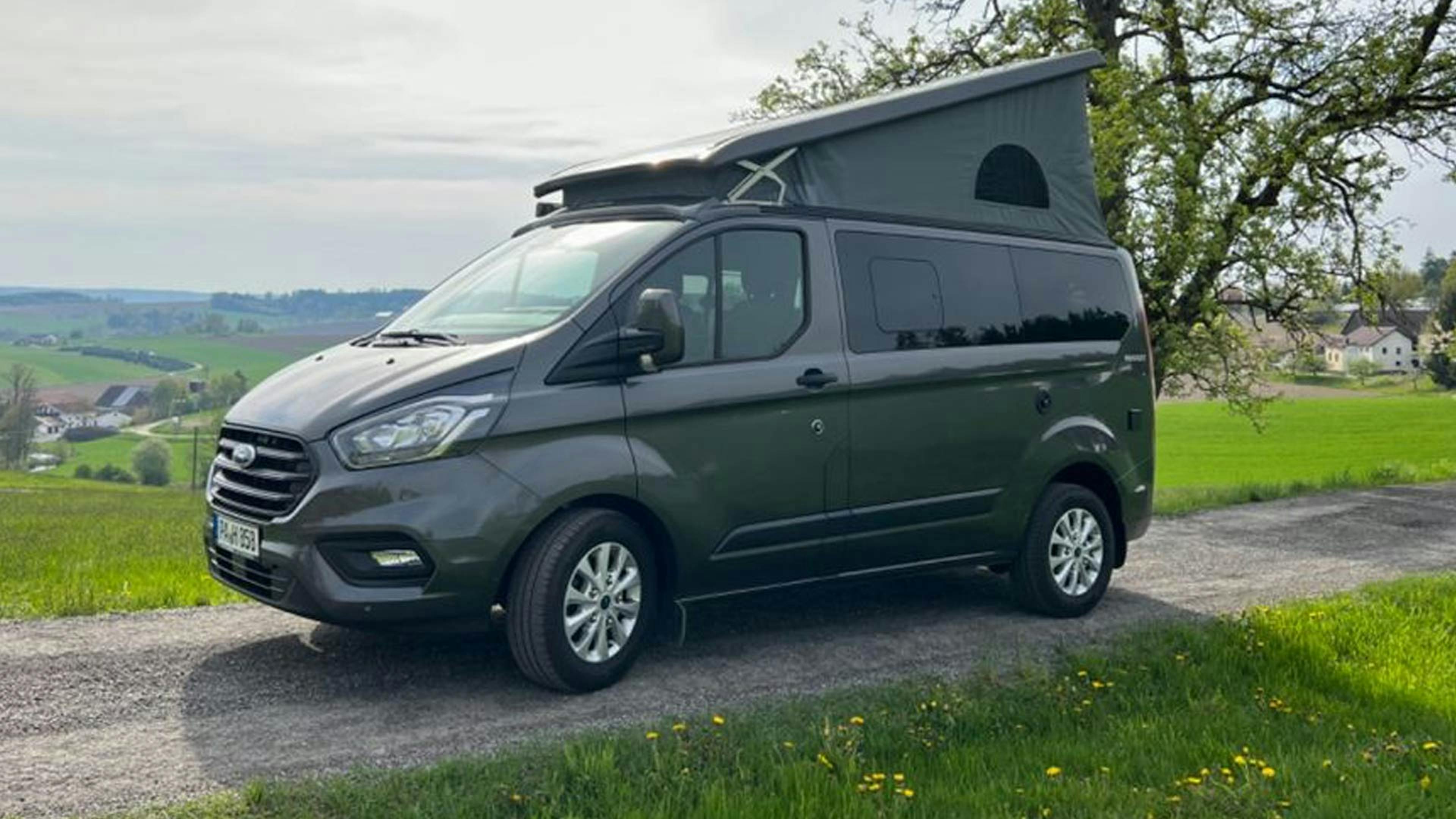 Ein grauer Ford Transit Custom Nugget Camper steht auf einem Feldweg.