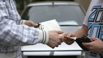 Sicherheit beim Autokauf: Eine Person übergibt einer anderen Geld und erhält im Gegenzug Fahrzeugpapiere und Autoschlüssel