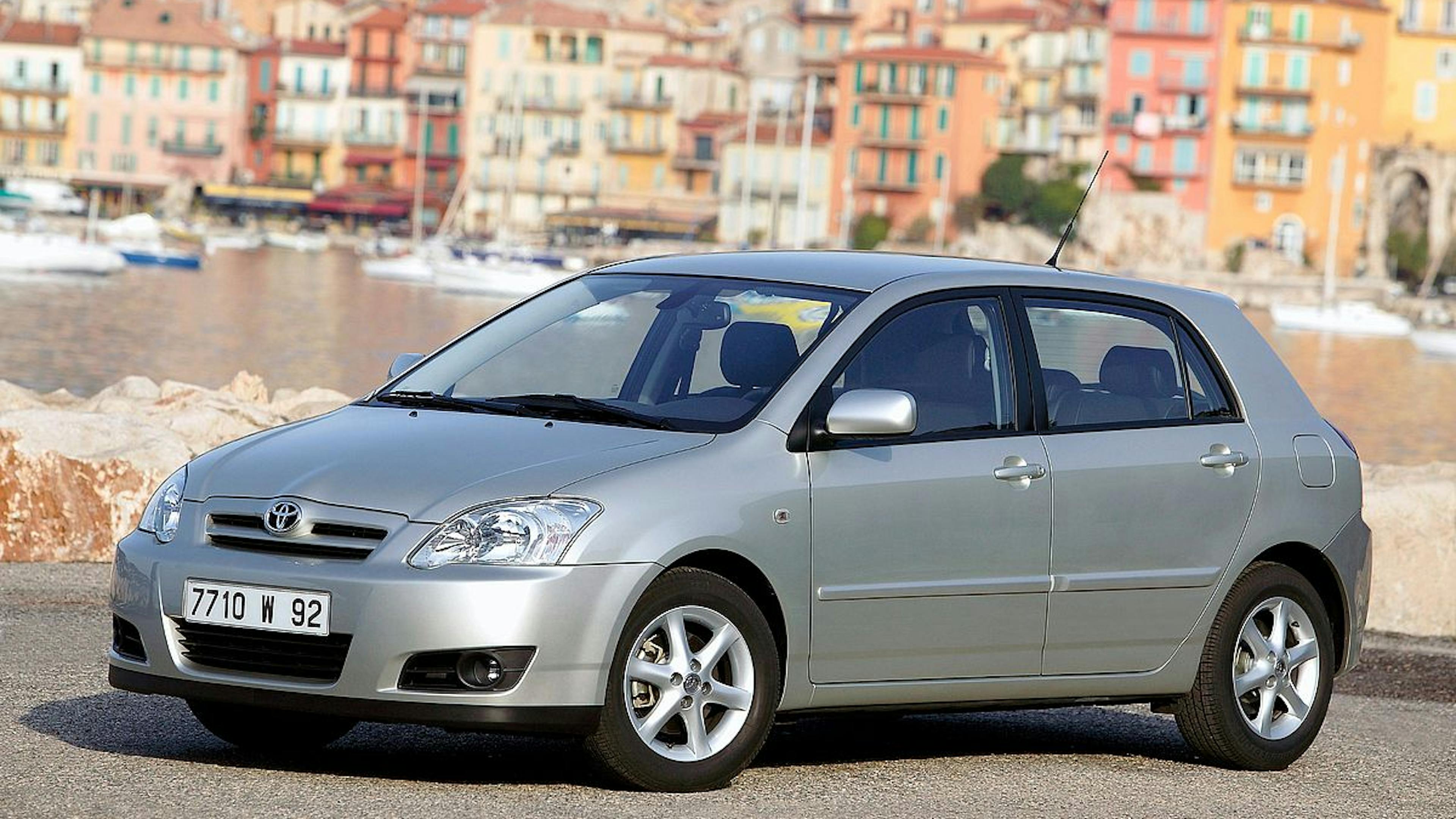 Ein silberner Toyota Corolla steht vor einer mediterranen Stadtkulisse