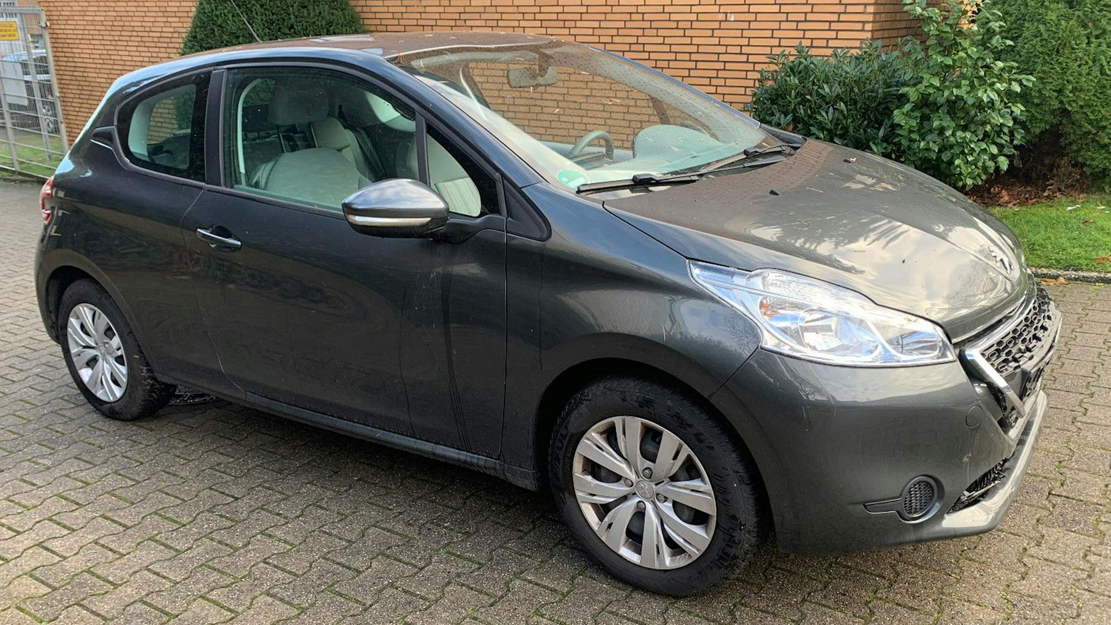 Ein grauer Peugeot 208 steht in einer Einfahrt vor einem Haus.