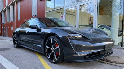 Ein schwarzes Porsche-Taycan-Elektroauto mit Allradantrieb steht vor einem Gebäude mit großen Fenstern.