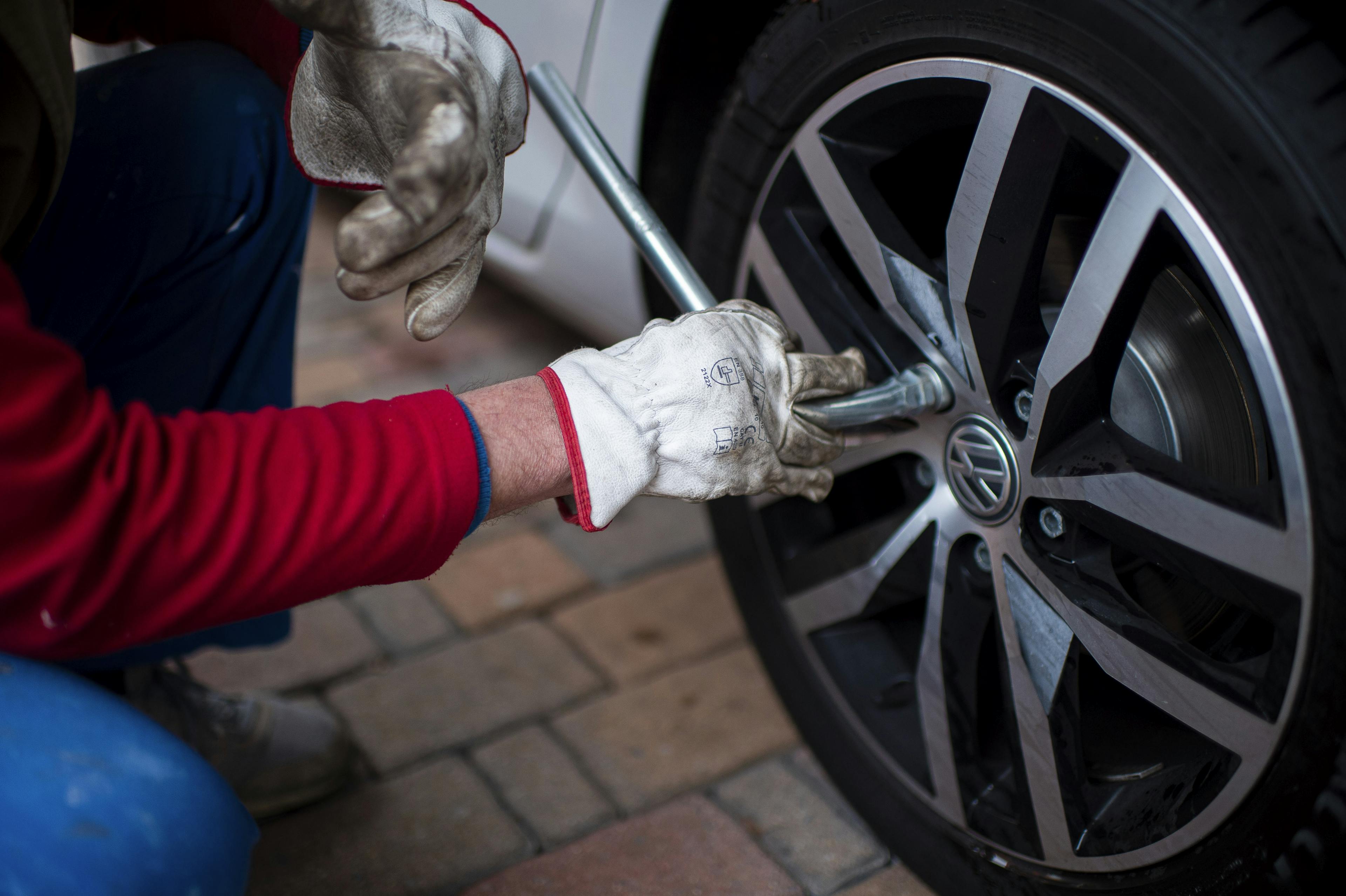Eine Person wechselt mit Handschuhen den Autoreifen und zieht mit einem Werkzeug die Schrauben an.